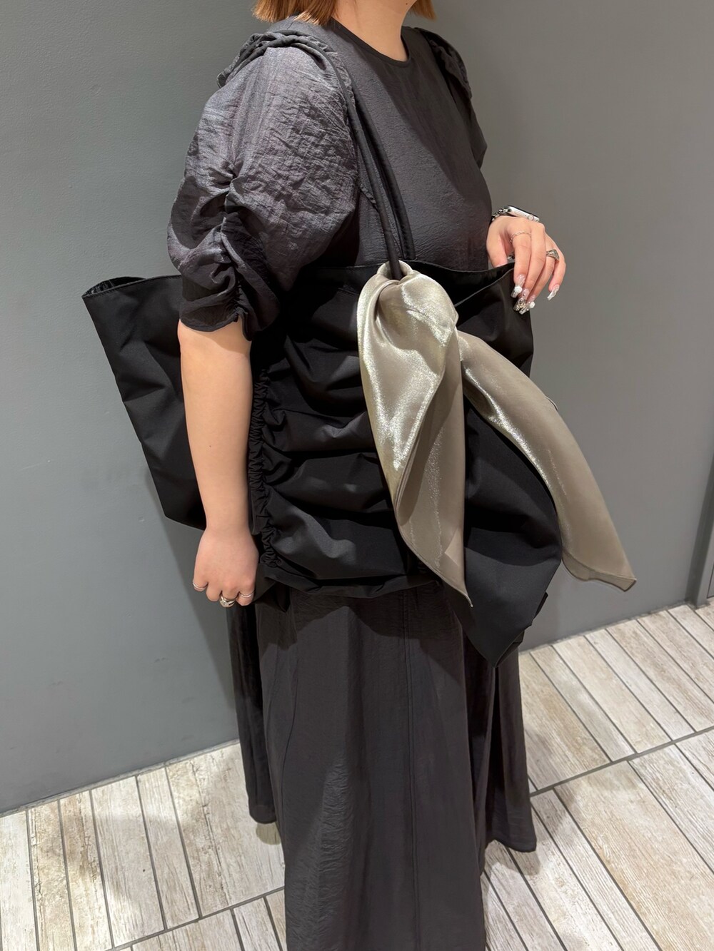 ブラック系のショルダーバッグ、ブルー系のデニムパンツ、グレー系のワンピースを着用したレディースの春コーディネートの9枚目の写真