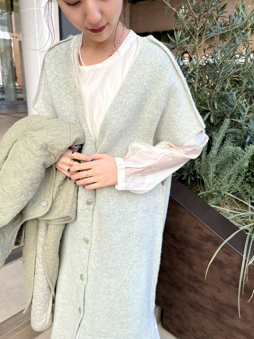 グリーン系のノーカラーコート、ホワイト系のワンピース、シルバー系のネックレスを着用したレディースの冬コーディネートの3枚目の写真