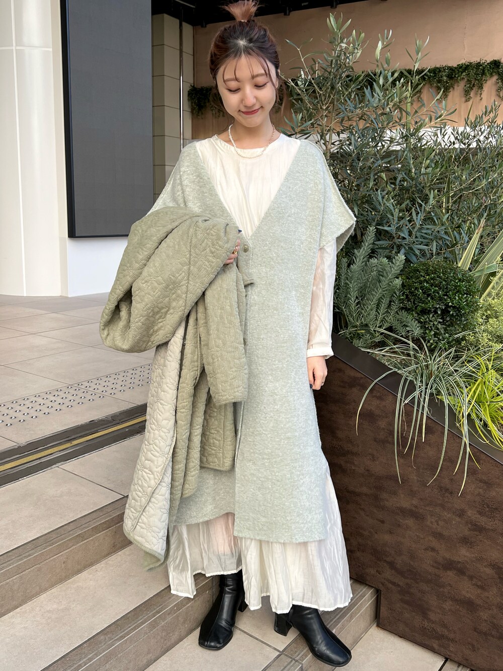 グリーン系のノーカラーコート、ホワイト系のワンピース、シルバー系のネックレスを着用したレディースの冬コーディネートの2枚目の写真
