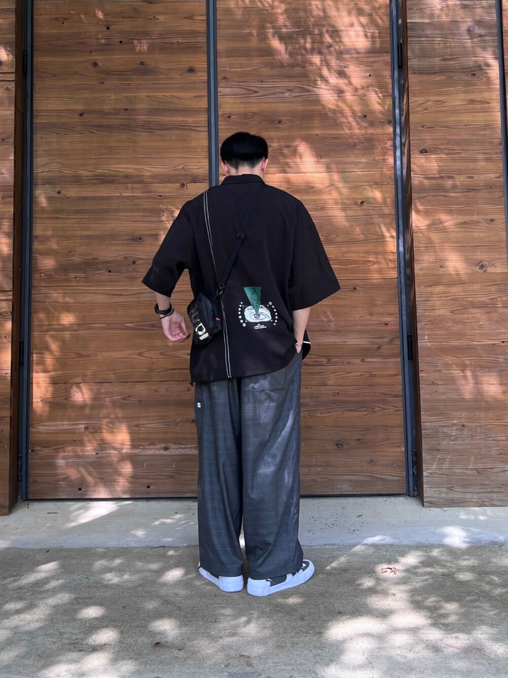 グレー系のチノパンツ、ブラック系のポロシャツ、グレー系のスニーカーを着用したメンズの夏コーディネートの2枚目の写真