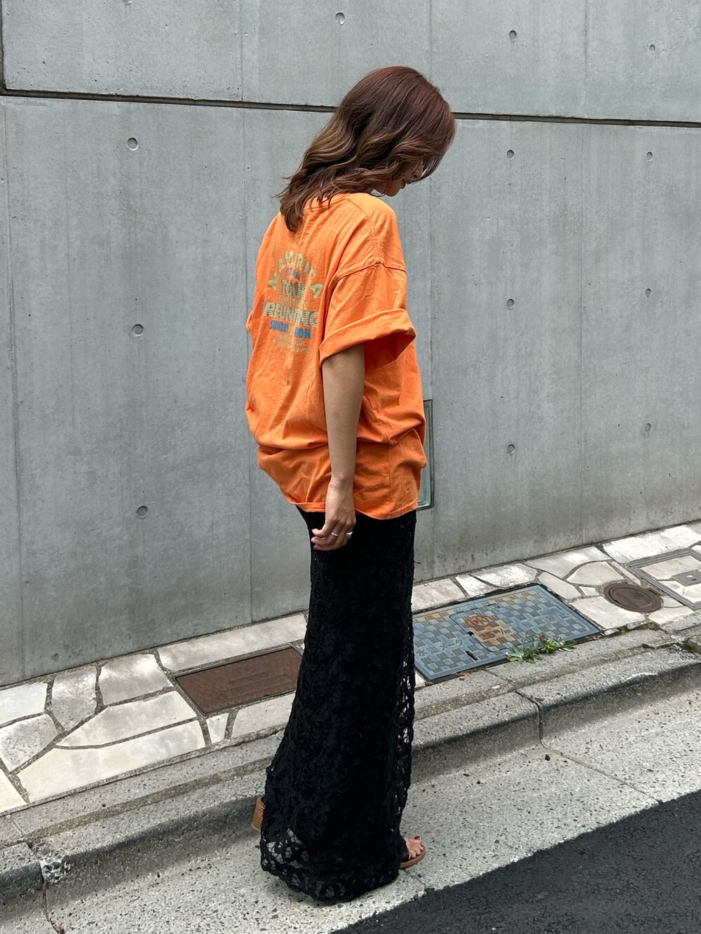 オレンジ系のTシャツ/カットソー、ブラック系のスカート、ブラック系のサンダルを着用したレディースの夏コーディネートの3枚目の写真