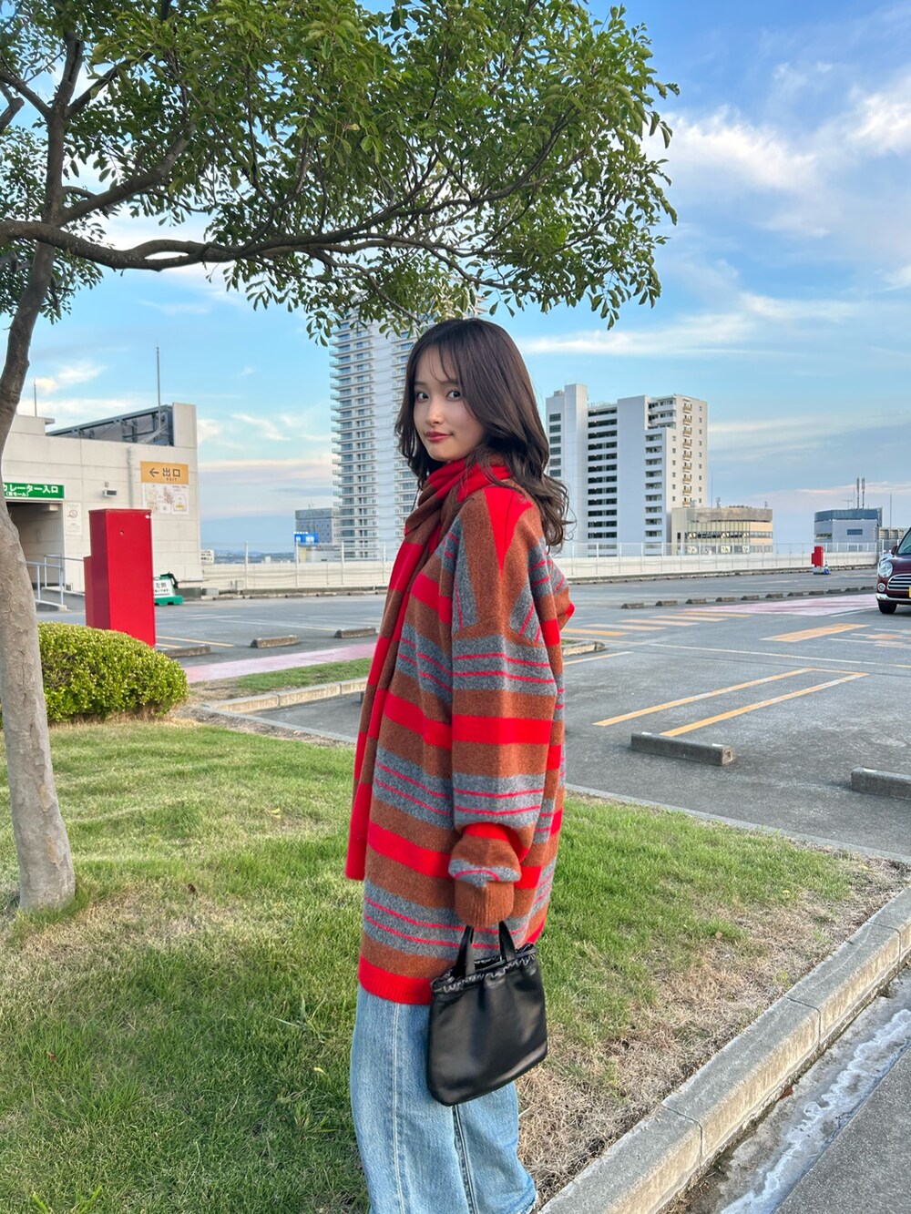 レッド系のニット/セーター、ブルー系のデニムパンツ、ブラック系のショルダーバッグを着用したレディースの秋コーディネートの6枚目の写真