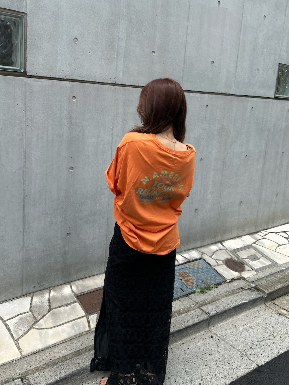 オレンジ系のTシャツ/カットソー、ブラック系のスカート、ブラック系のサンダルを着用したレディースの夏コーディネートの5枚目の写真