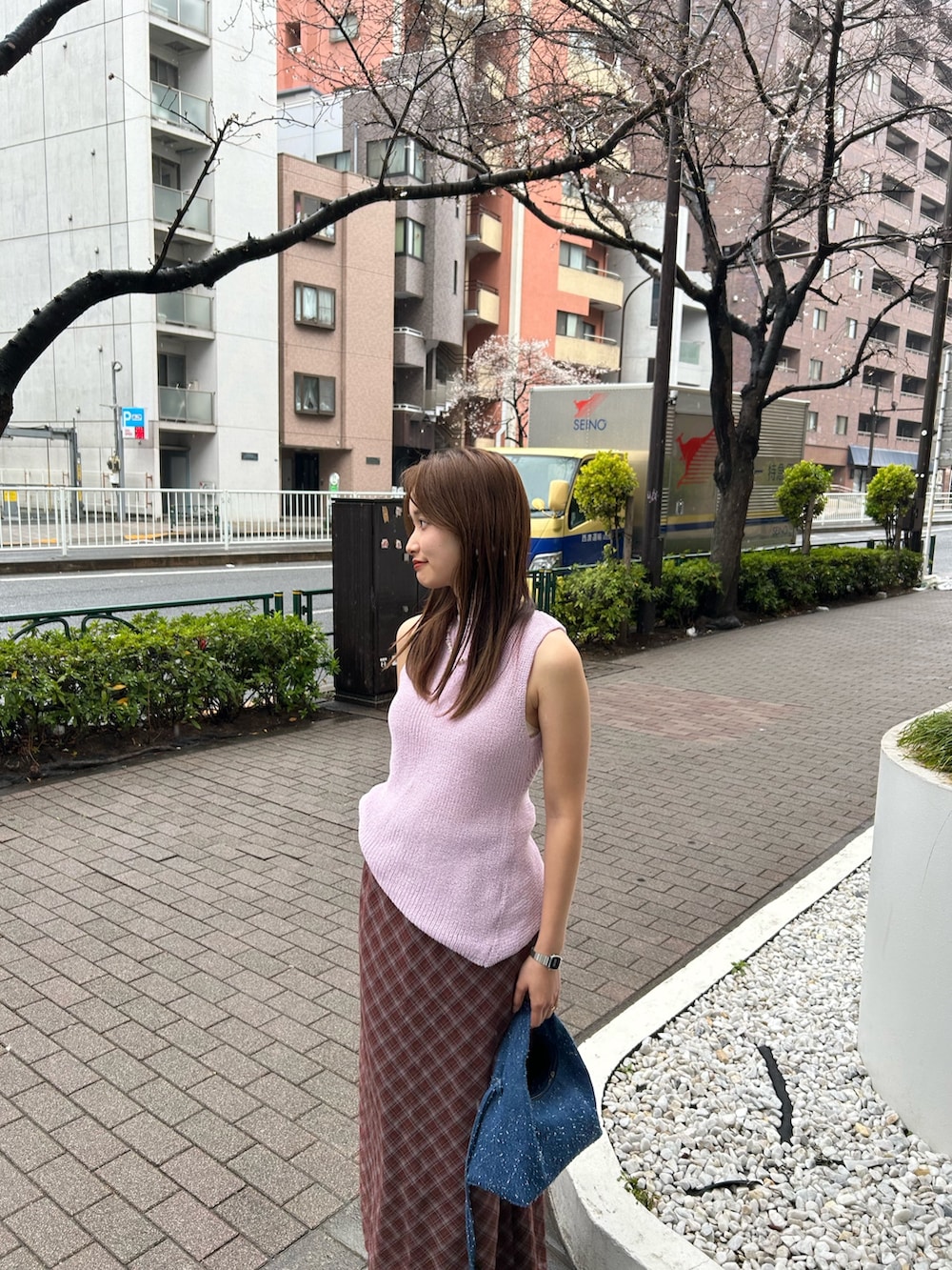 ブルー系のハンドバッグ、ブラウン系のスカート、シルバー系のネックレスを着用したレディースの春コーディネートの4枚目の写真