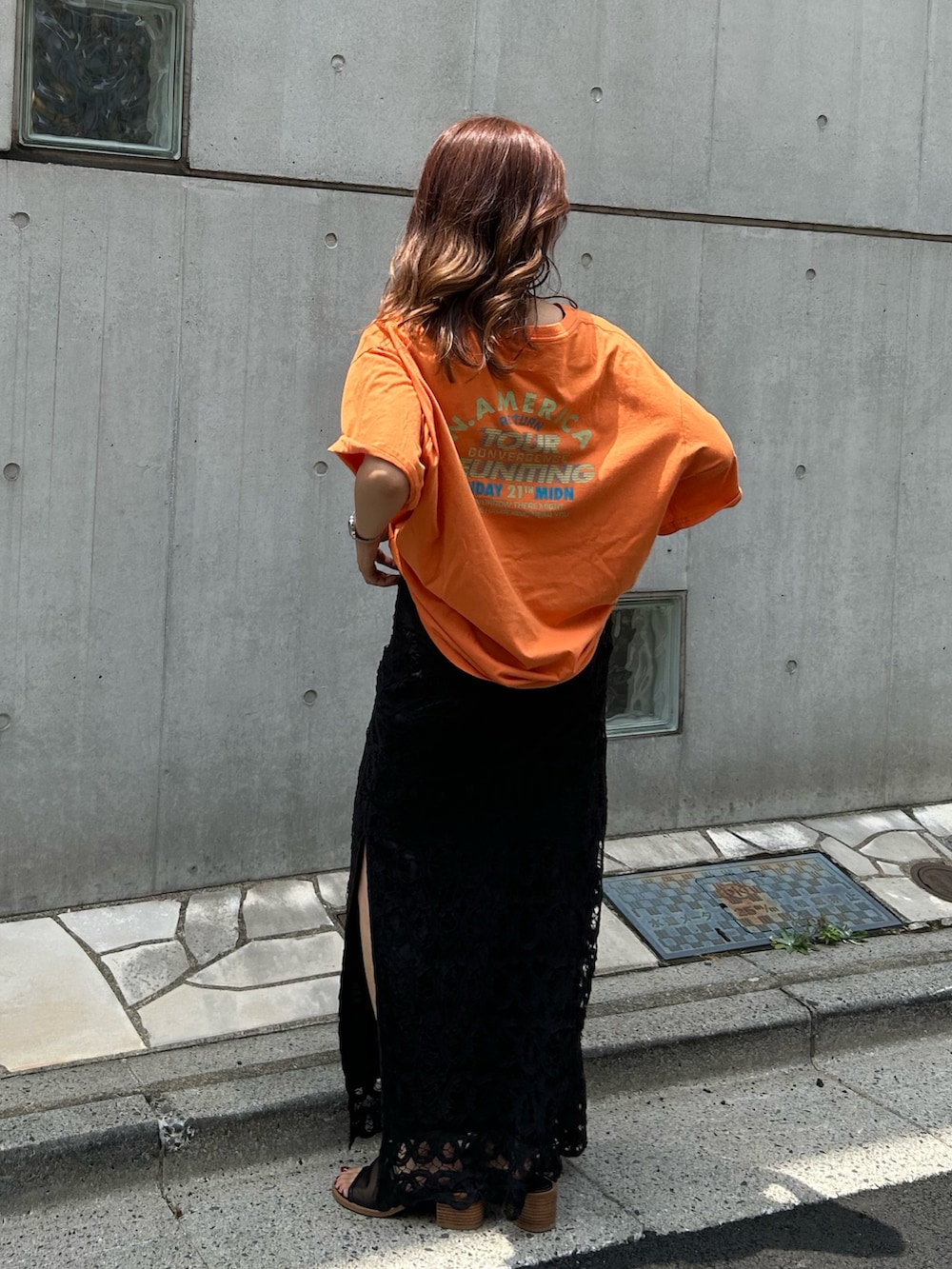オレンジ系のTシャツ/カットソー、ブラック系のスカート、ブラック系のサンダルを着用したレディースの夏コーディネートの6枚目の写真