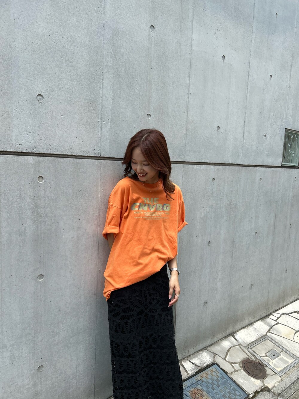 オレンジ系のTシャツ/カットソー、ブラック系のスカート、ブラック系のサンダルを着用したレディースの夏コーディネートの4枚目の写真