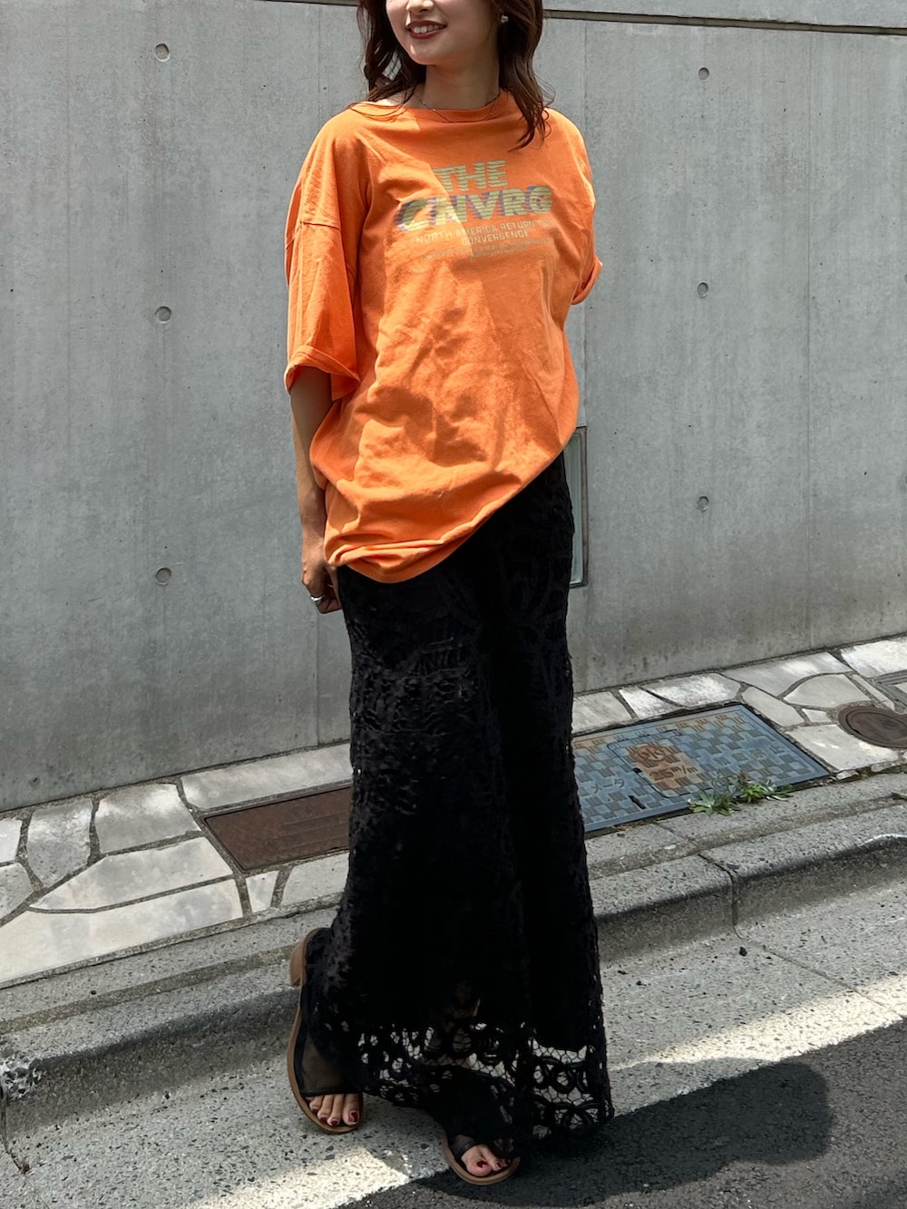 オレンジ系のTシャツ/カットソー、ブラック系のスカート、ブラック系のサンダルを着用したレディースの夏コーディネートの7枚目の写真