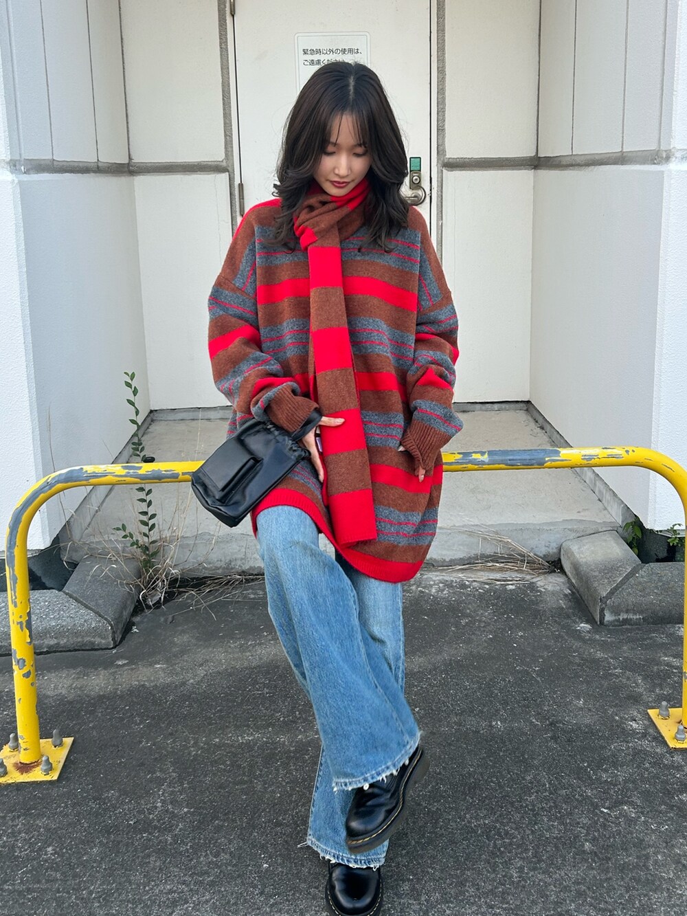 レッド系のニット/セーター、ブルー系のデニムパンツ、ブラック系のショルダーバッグを着用したレディースの秋コーディネートの3枚目の写真