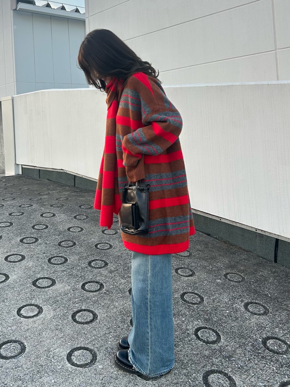 レッド系のニット/セーター、ブルー系のデニムパンツ、ブラック系のショルダーバッグを着用したレディースの秋コーディネートの2枚目の写真