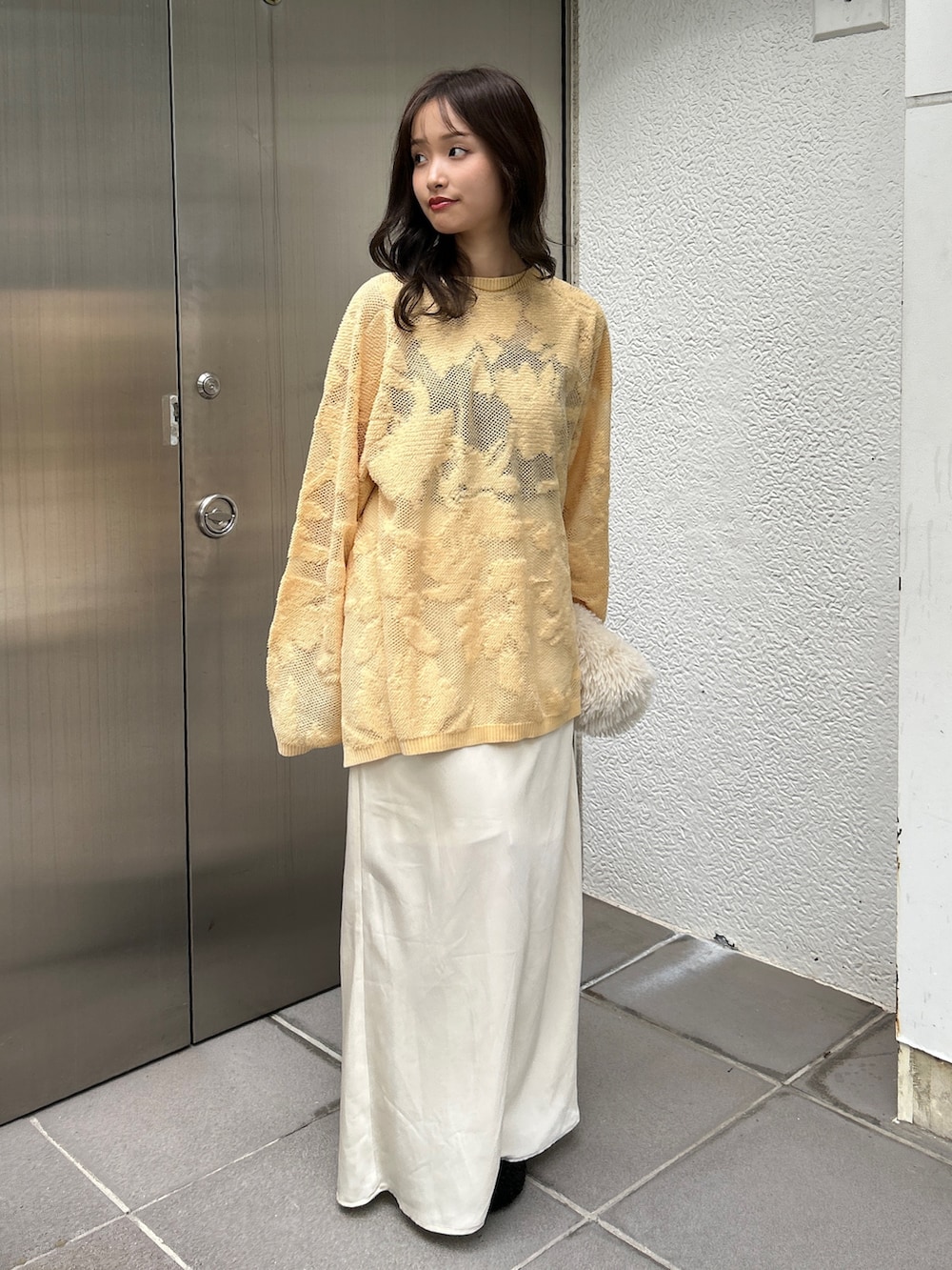 ブラック系のスリッポン、ホワイト系のハンドバッグ、イエロー系のニット/セーターを着用したレディースの冬コーディネートの2枚目の写真