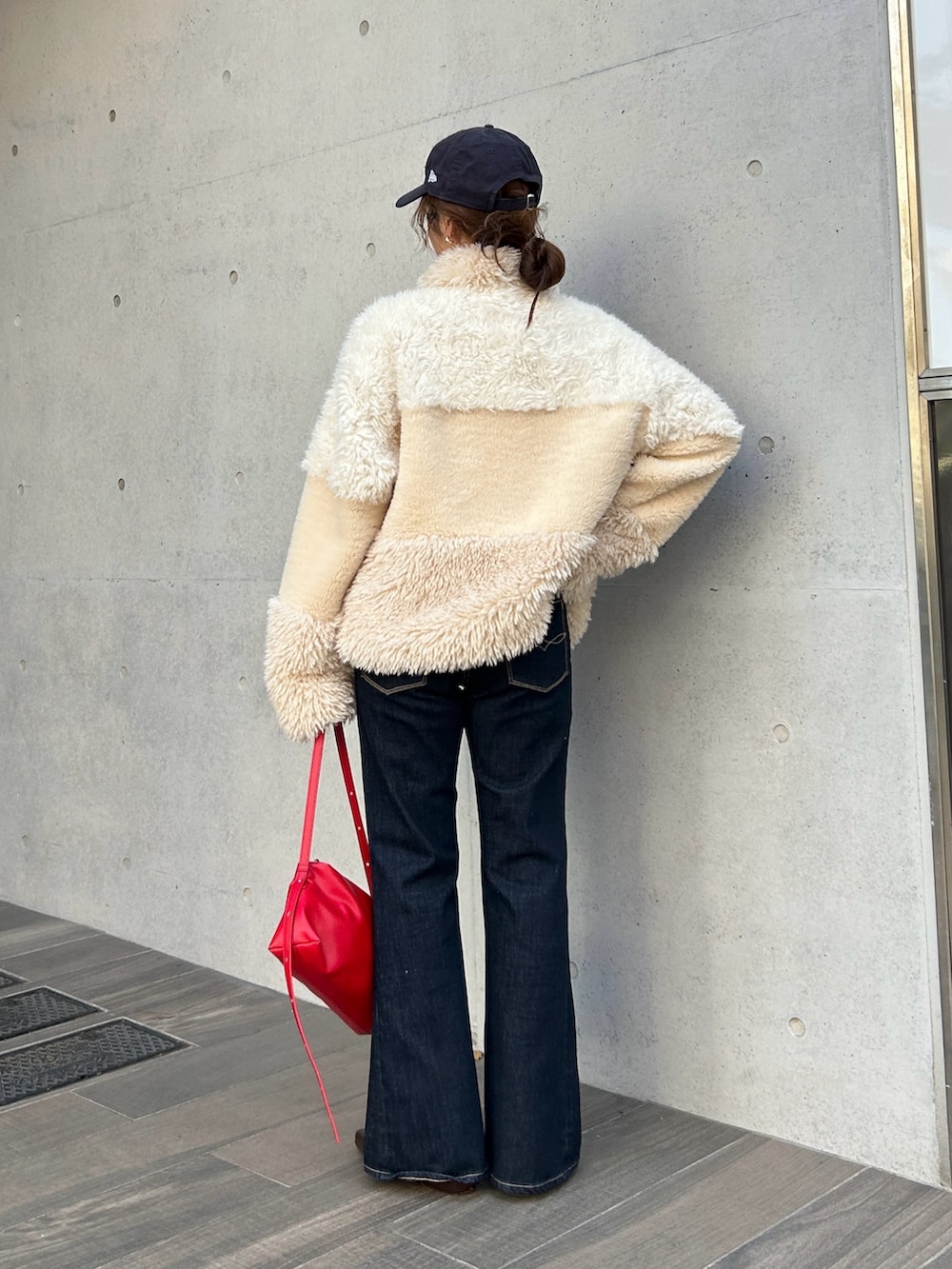 ホワイト系のブルゾン、レッド系のハンドバッグ、ブルー系のデニムパンツを着用したレディースの秋コーディネートの3枚目の写真