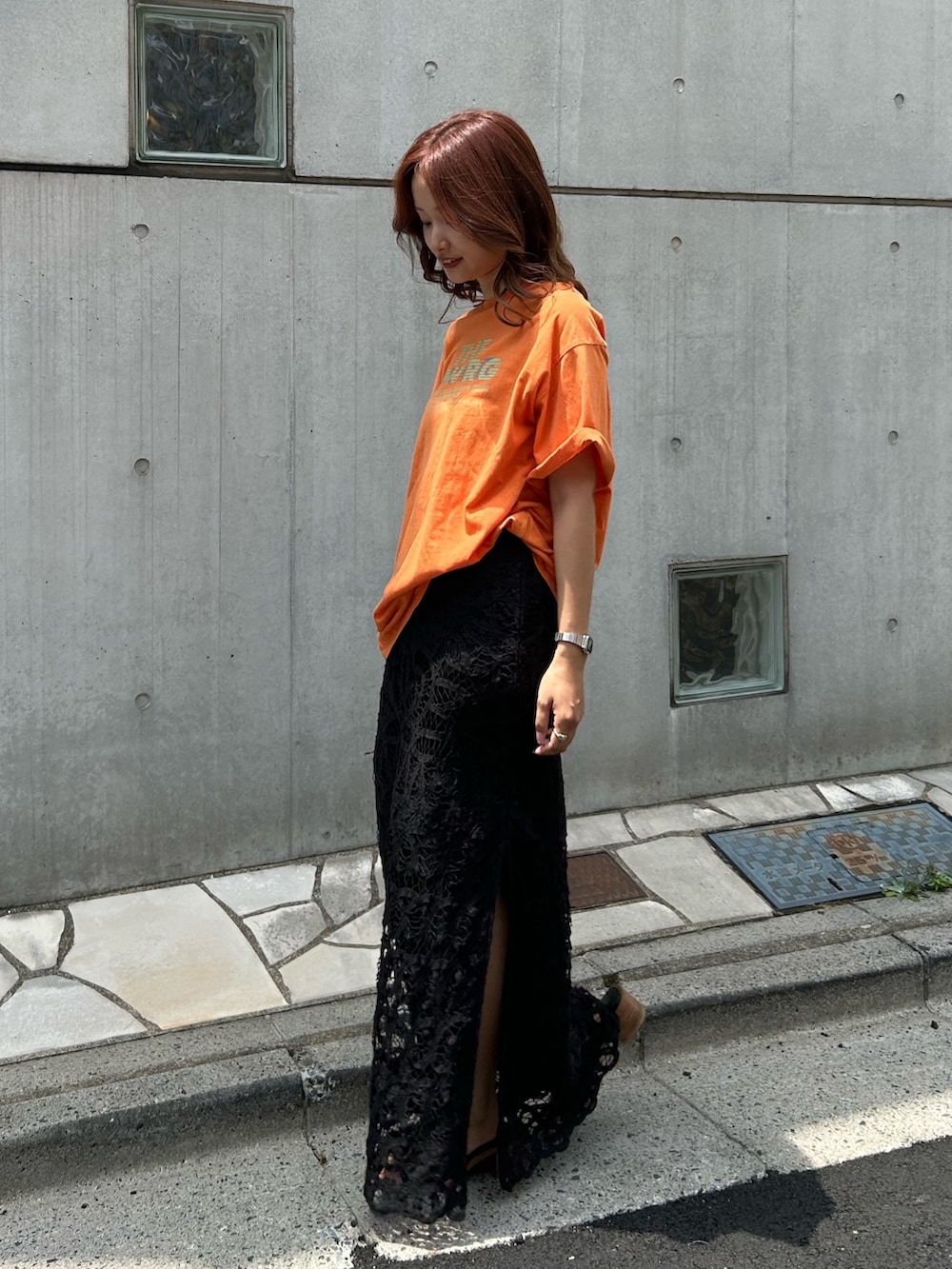 オレンジ系のTシャツ/カットソー、ブラック系のスカート、ブラック系のサンダルを着用したレディースの夏コーディネートの2枚目の写真