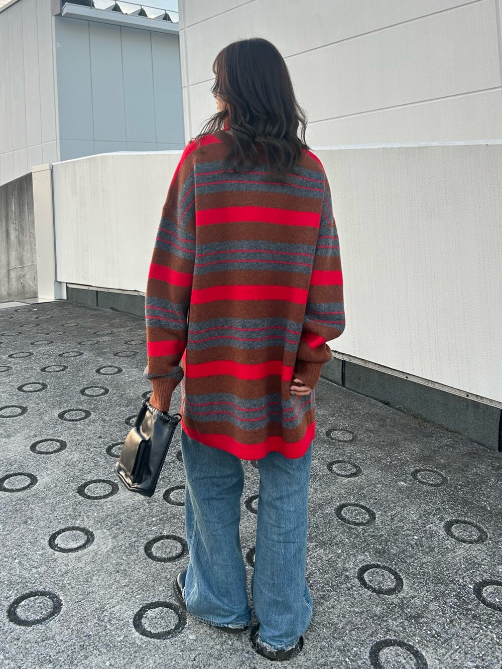 レッド系のニット/セーター、ブルー系のデニムパンツ、ブラック系のショルダーバッグを着用したレディースの秋コーディネートの4枚目の写真