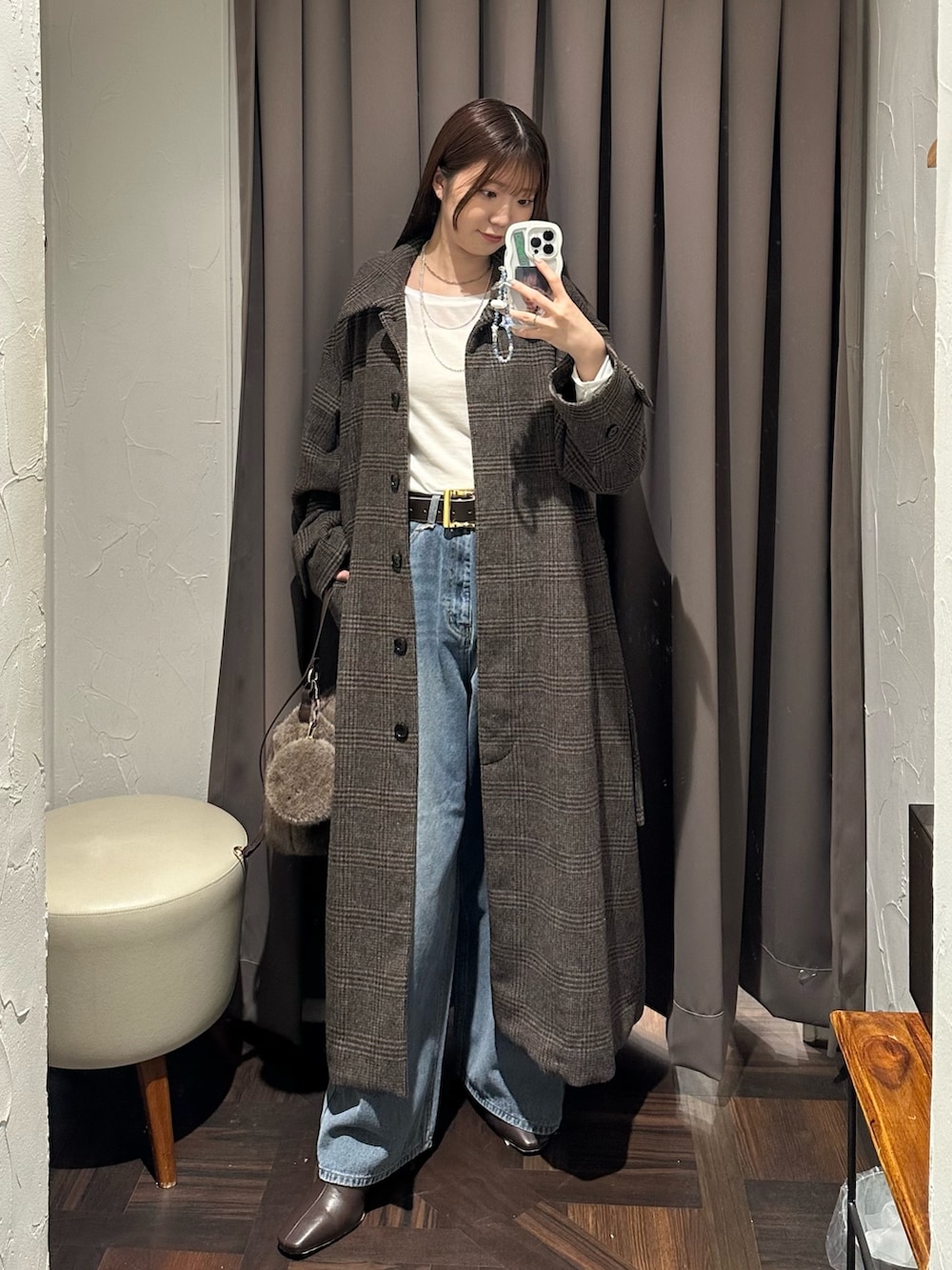 ブラウン系のステンカラーコート、ブラウン系のハンドバッグ、ブルー系のデニムパンツを着用したレディースの秋コーディネートの2枚目の写真