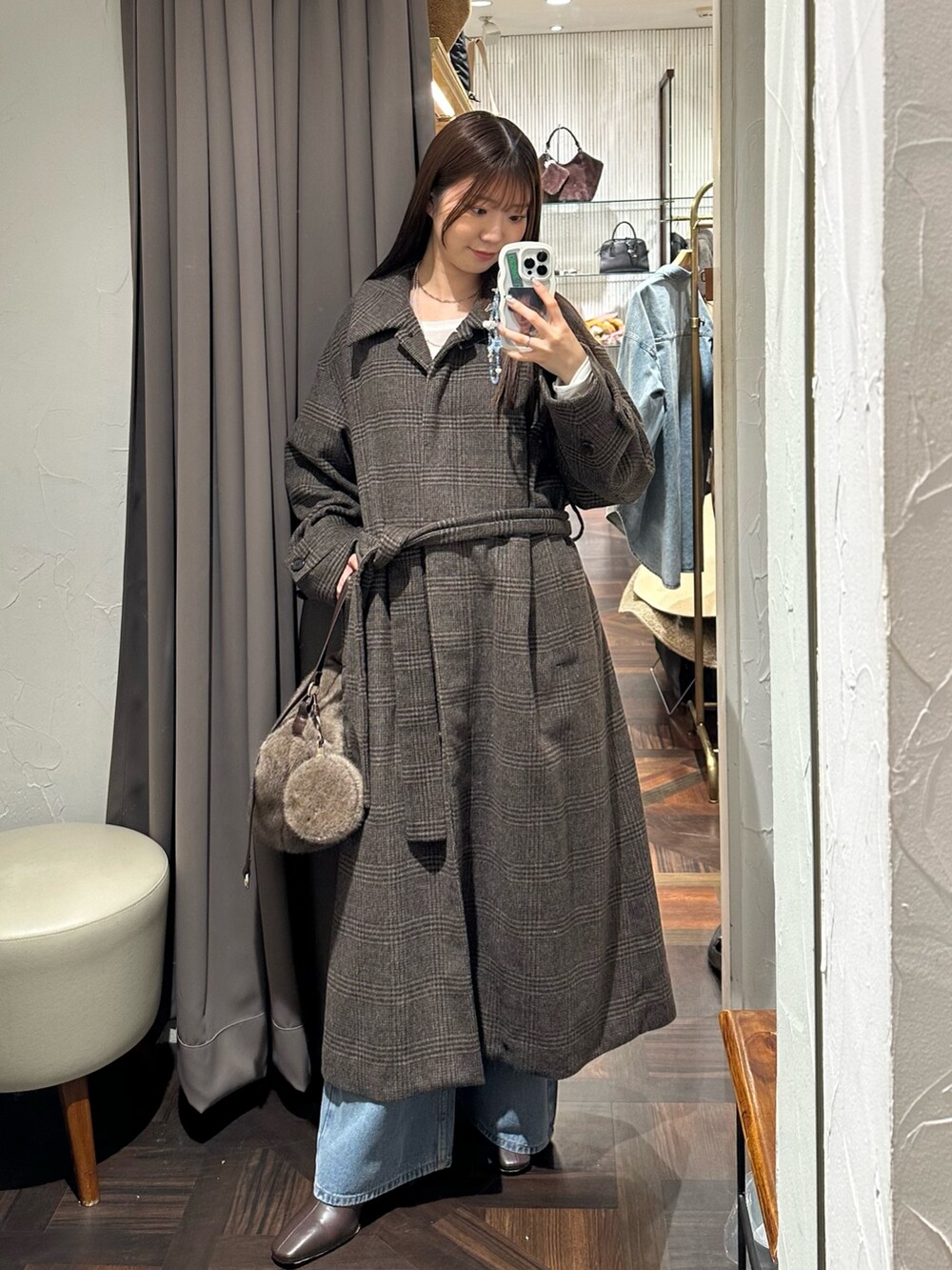 ブラウン系のステンカラーコート、ブラウン系のハンドバッグ、ブルー系のデニムパンツを着用したレディースの秋コーディネートの3枚目の写真