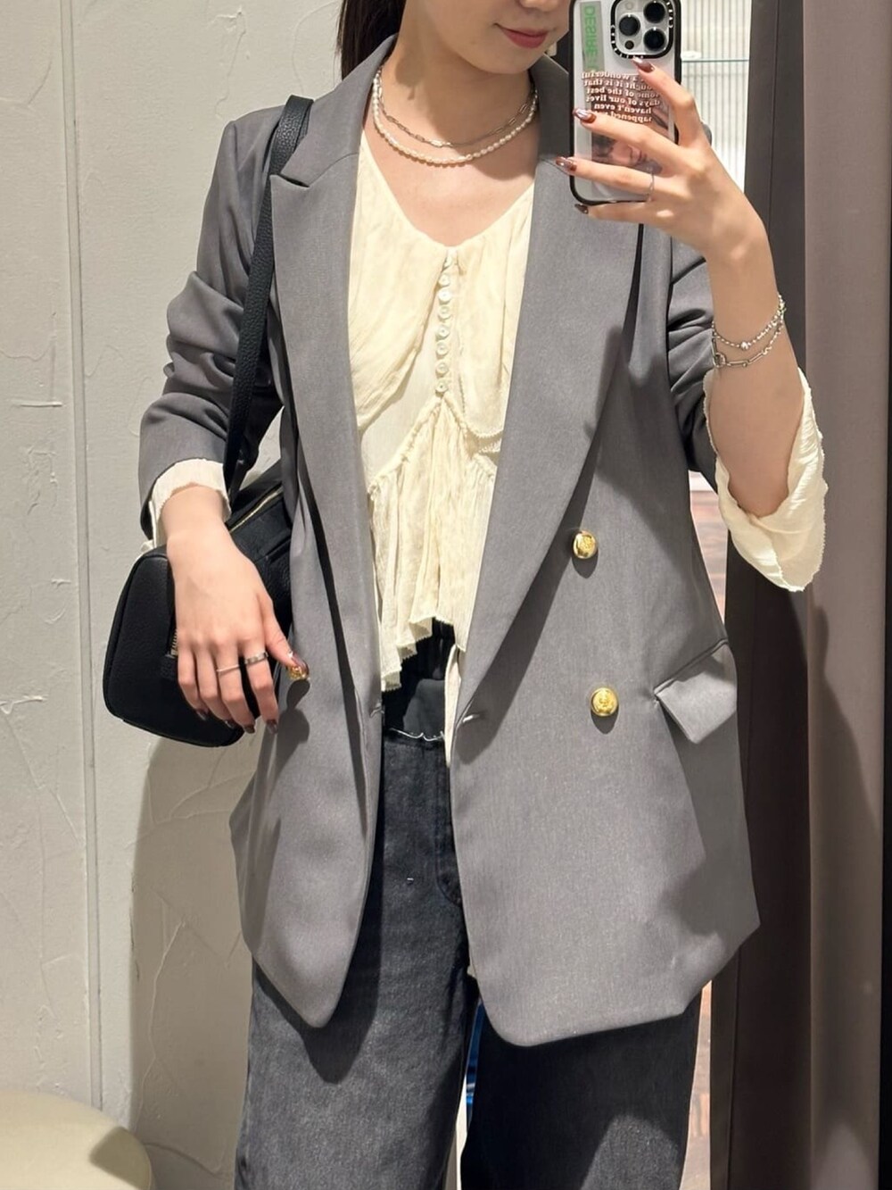 グレー系のテーラードジャケット、ブラック系のデニムパンツ、ブラック系のパンプスを着用したレディースの秋コーディネートの2枚目の写真