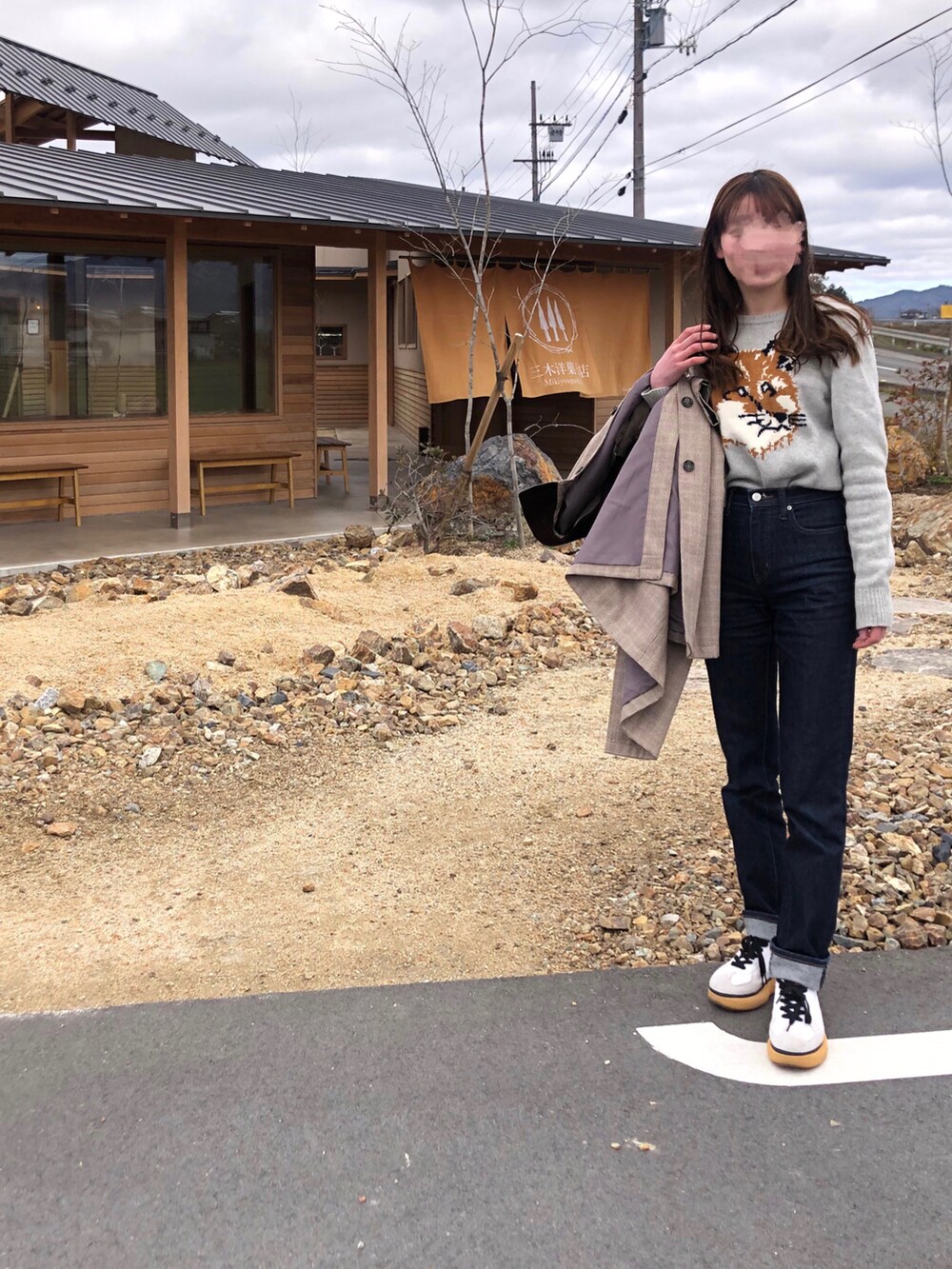 ブラウン系のステンカラーコート、ブルー系のデニムパンツ、ブラック系のボストンバッグを着用したレディースの冬コーディネートの2枚目の写真