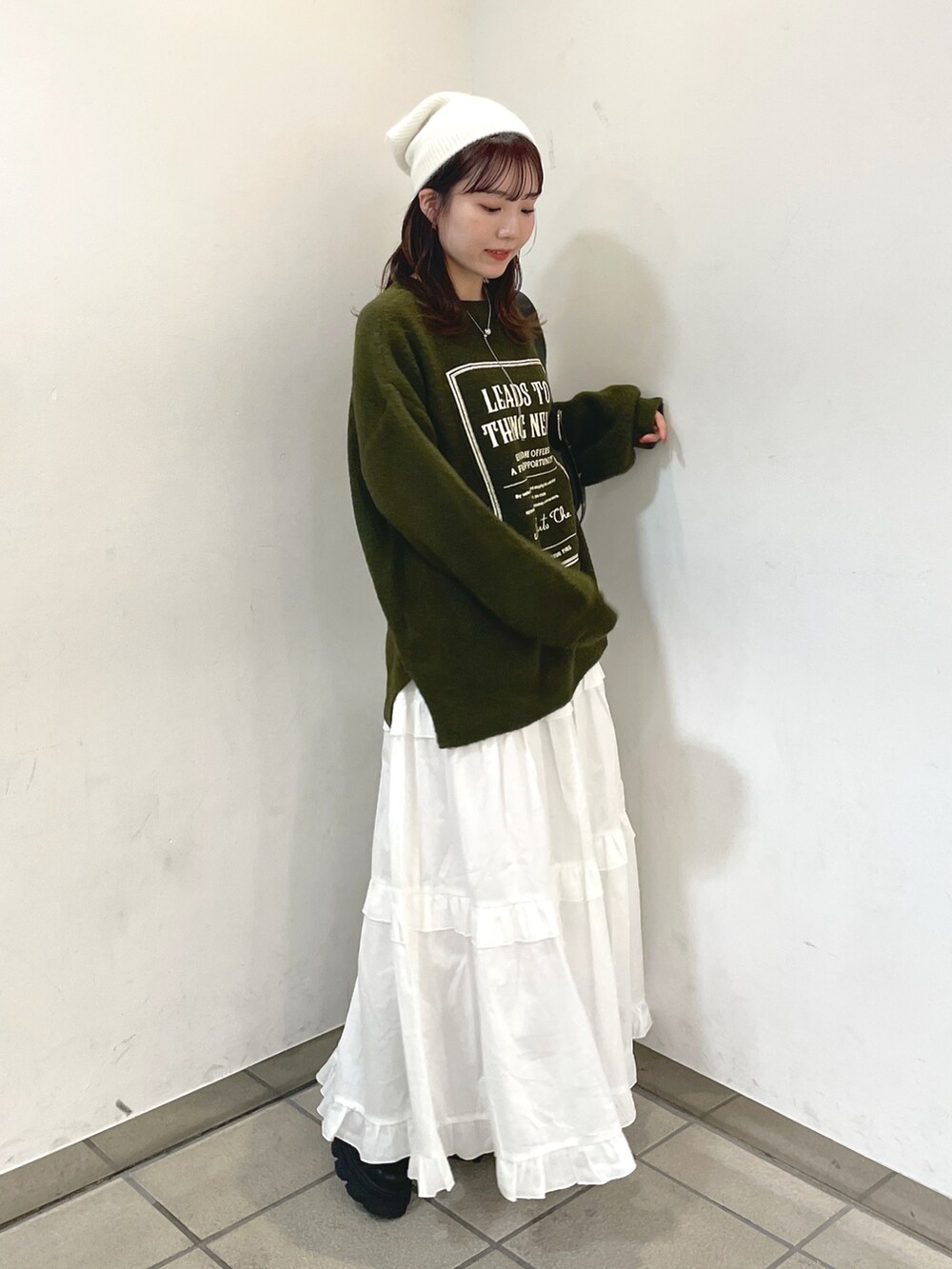 グリーン系のニット/セーター、ホワイト系のスカート、ブラック系のショルダーバッグを着用したレディースの秋コーディネートの2枚目の写真
