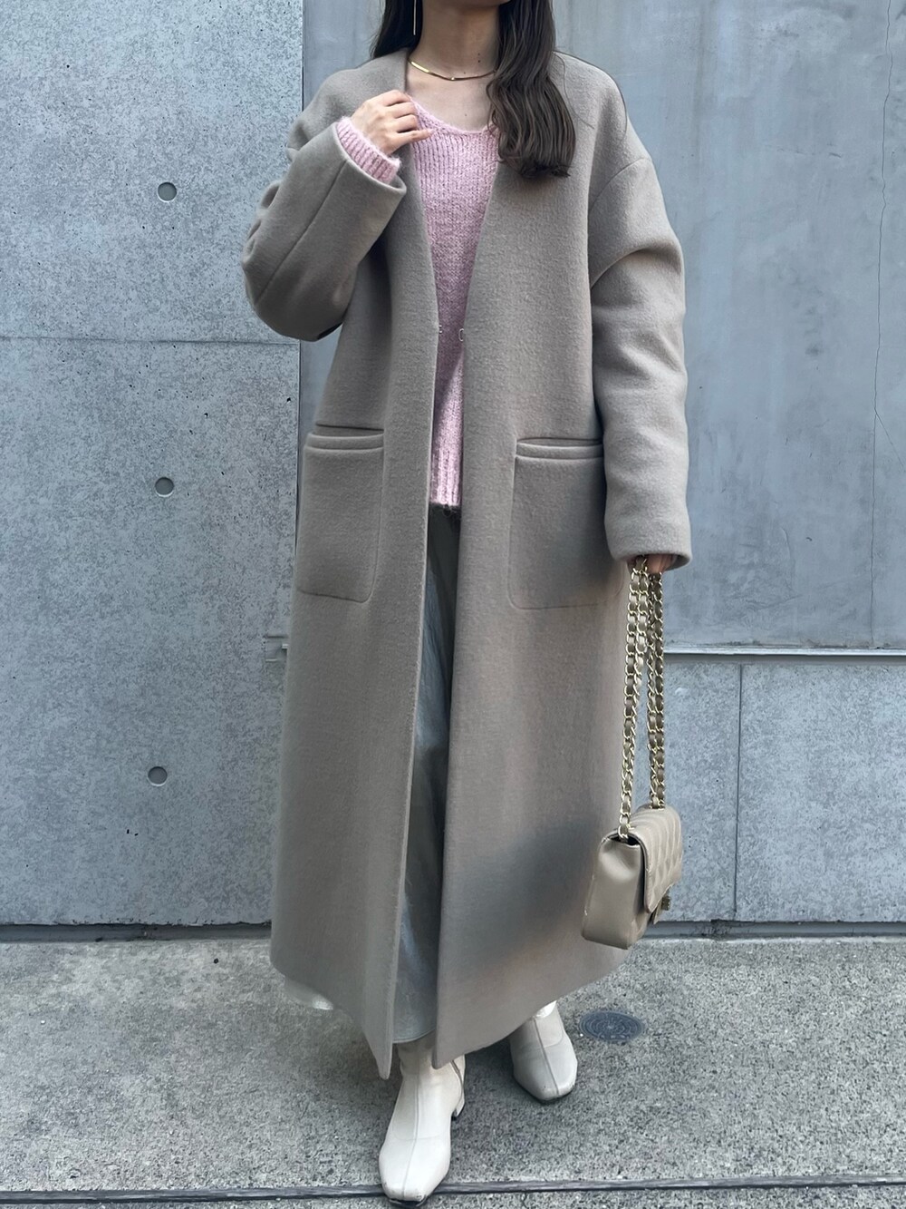 ベージュ系のノーカラーコート、ベージュ系のショルダーバッグ、ピンク系のニット/セーターを着用したレディースの冬コーディネートの2枚目の写真
