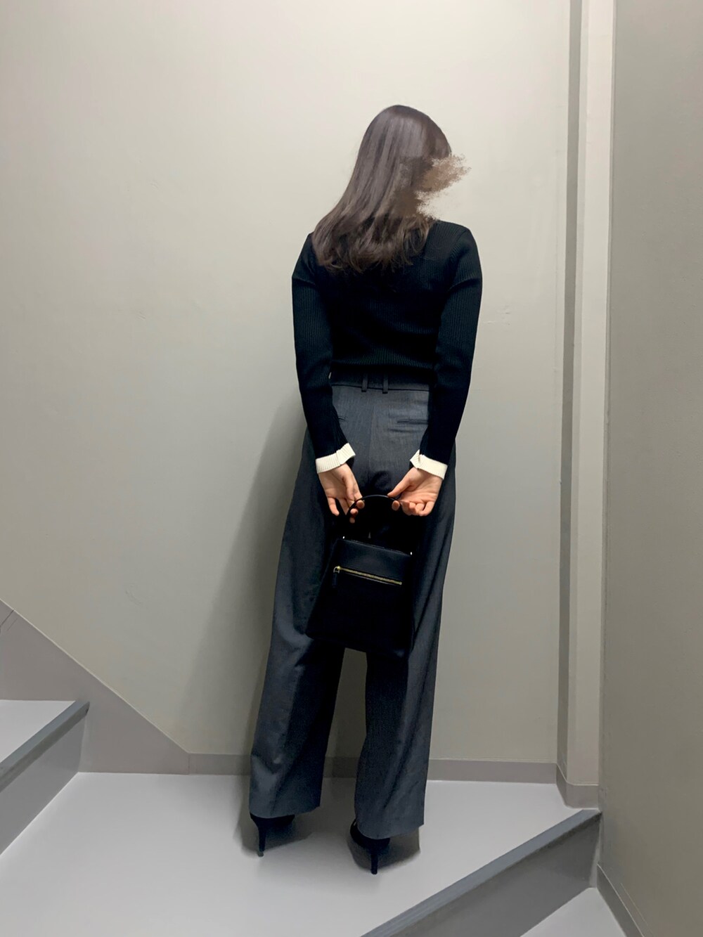 グレー系のパンツ、ブラック系のニット/セーター、ブラック系のハンドバッグを着用したレディースの冬コーディネートの2枚目の写真