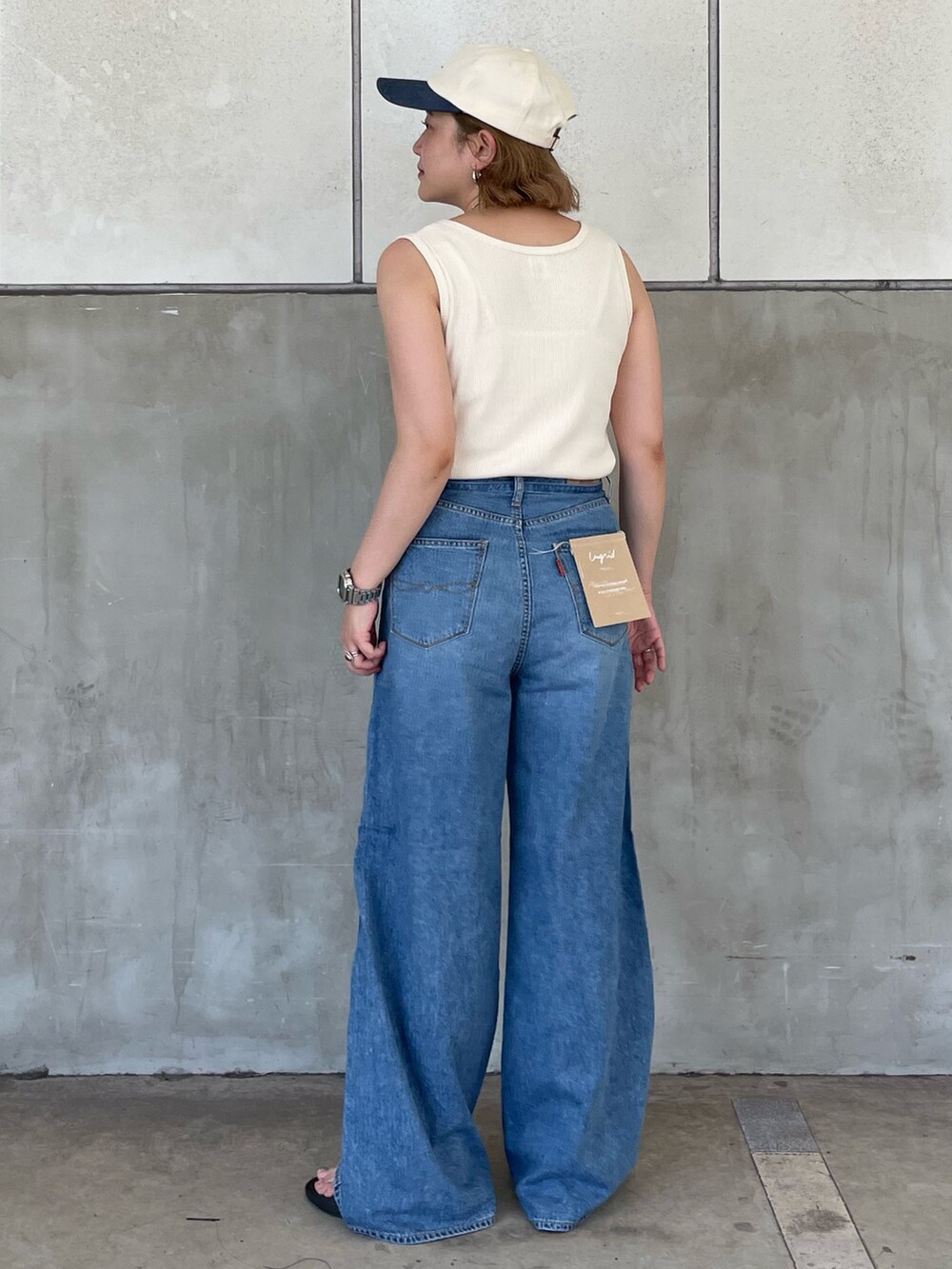 ブルー系のデニムパンツ、ホワイト系のタンクトップ、ホワイト系のキャップを着用したレディースの夏コーディネートの3枚目の写真