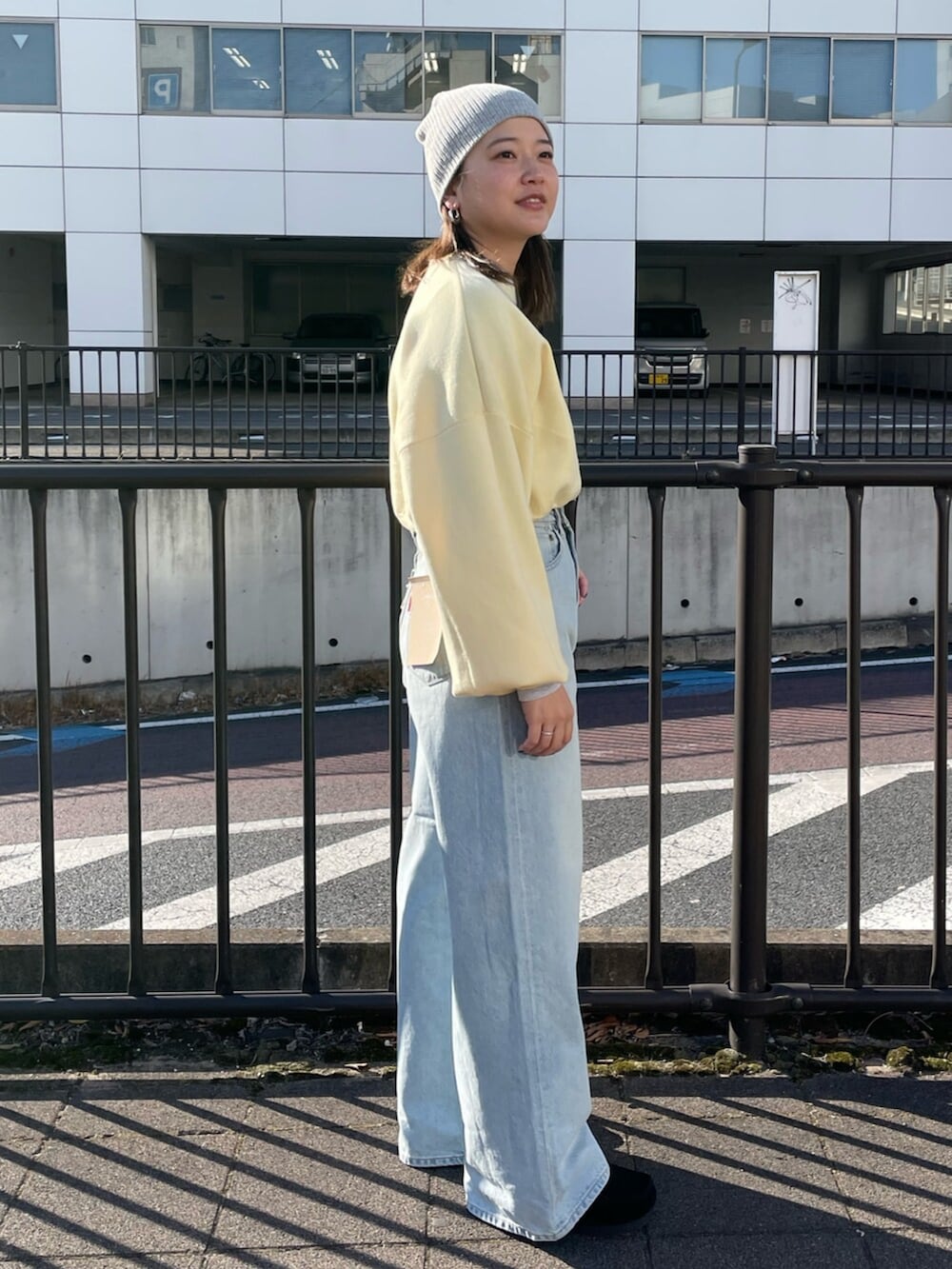 イエロー系のニット/セーター、ブルー系のデニムパンツ、グレー系のニットキャップ/ビーニーを着用したレディースの冬コーディネートの2枚目の写真