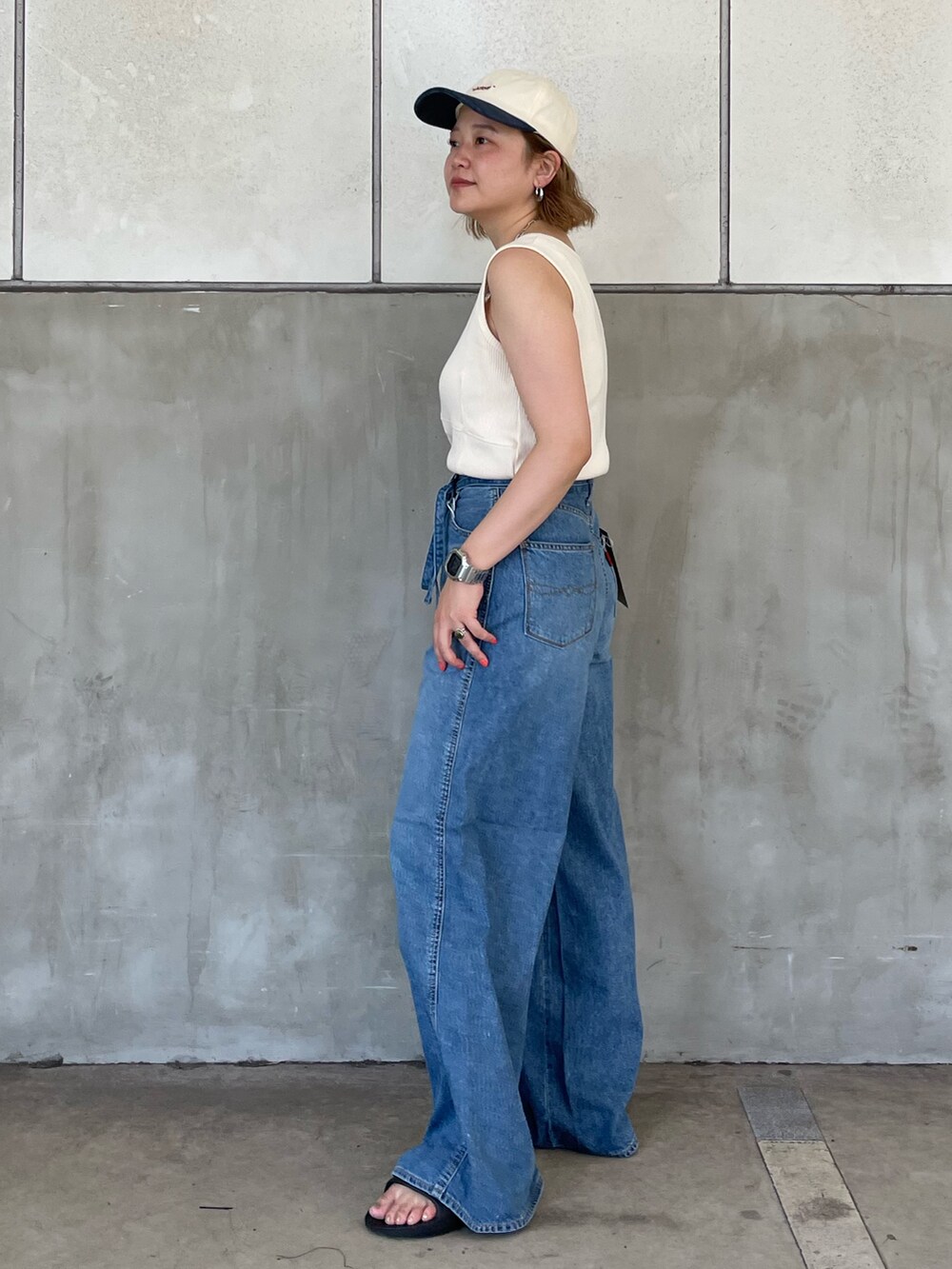 ブルー系のデニムパンツ、ホワイト系のタンクトップ、ホワイト系のキャップを着用したレディースの夏コーディネートの2枚目の写真