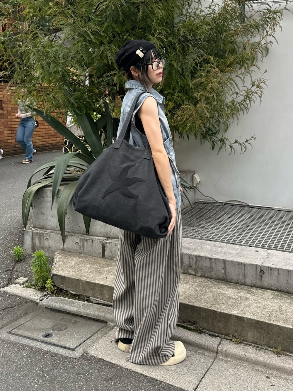 ブルー系のベスト、ブラック系のボストンバッグ、グレー系のスラックスを着用したレディースの夏コーディネートの2枚目の写真