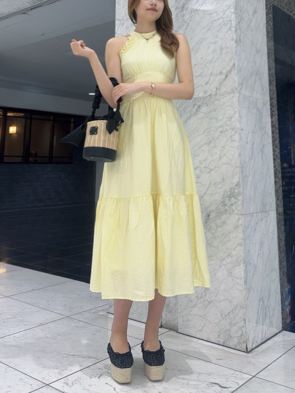 イエロー系のワンピース、ブラック系のかごバッグ、ブラック系のサンダルを着用したレディースの夏コーディネートの2枚目の写真
