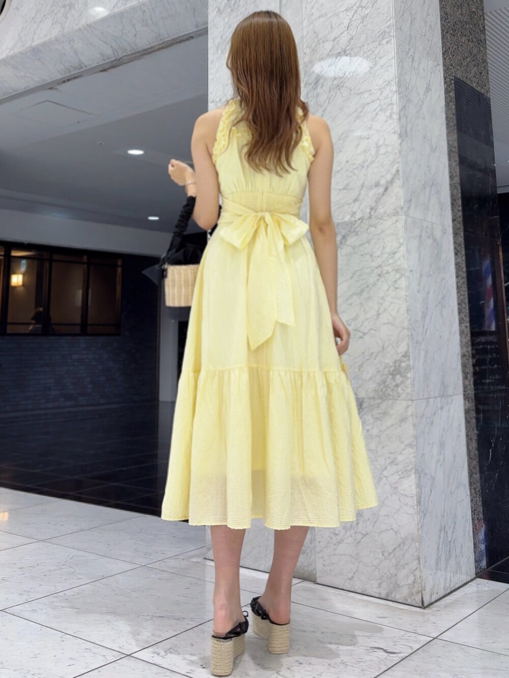 イエロー系のワンピース、ブラック系のかごバッグ、ブラック系のサンダルを着用したレディースの夏コーディネートの3枚目の写真