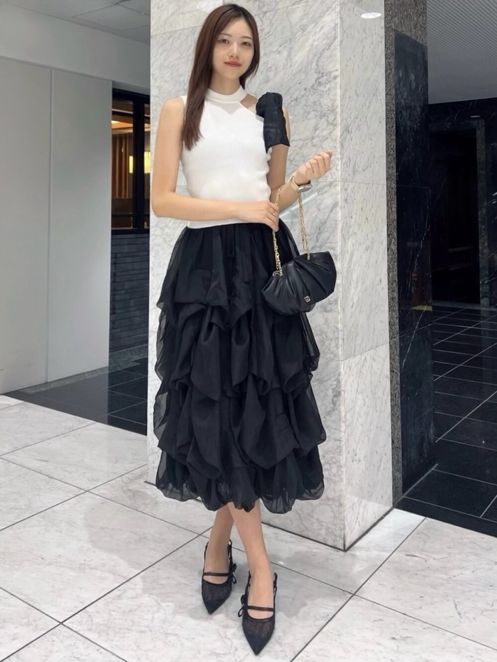 ブラック系のパンプス、ホワイト系のニット/セーター、ブラック系のスカートを着用したレディースの夏コーディネートの2枚目の写真