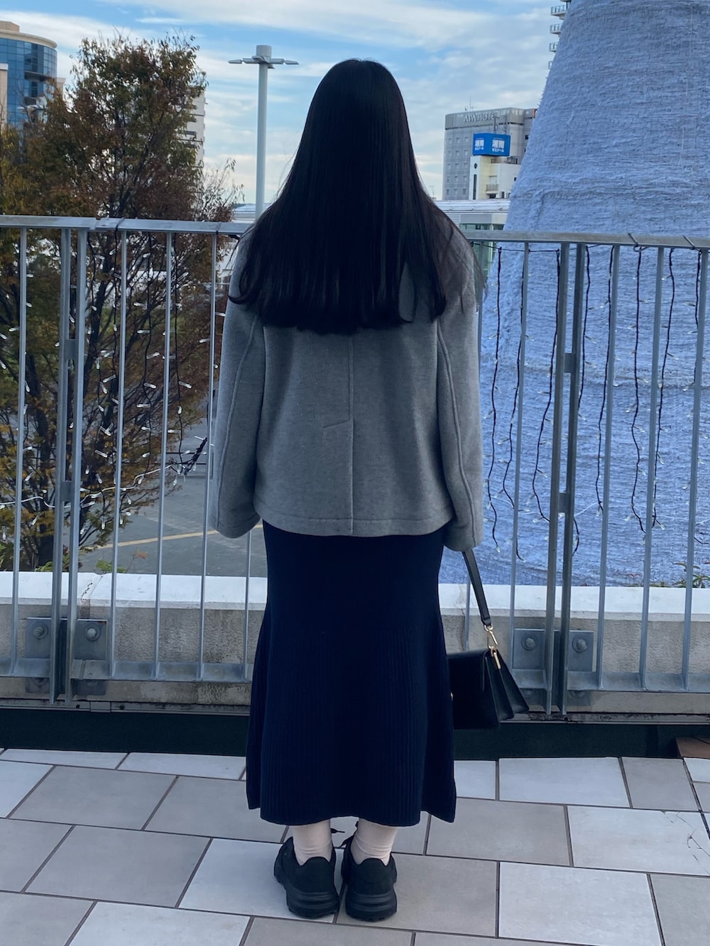 グレー系のピーコート、ブルー系のワンピース、ブラック系のバッグを着用したレディースの冬コーディネートの3枚目の写真