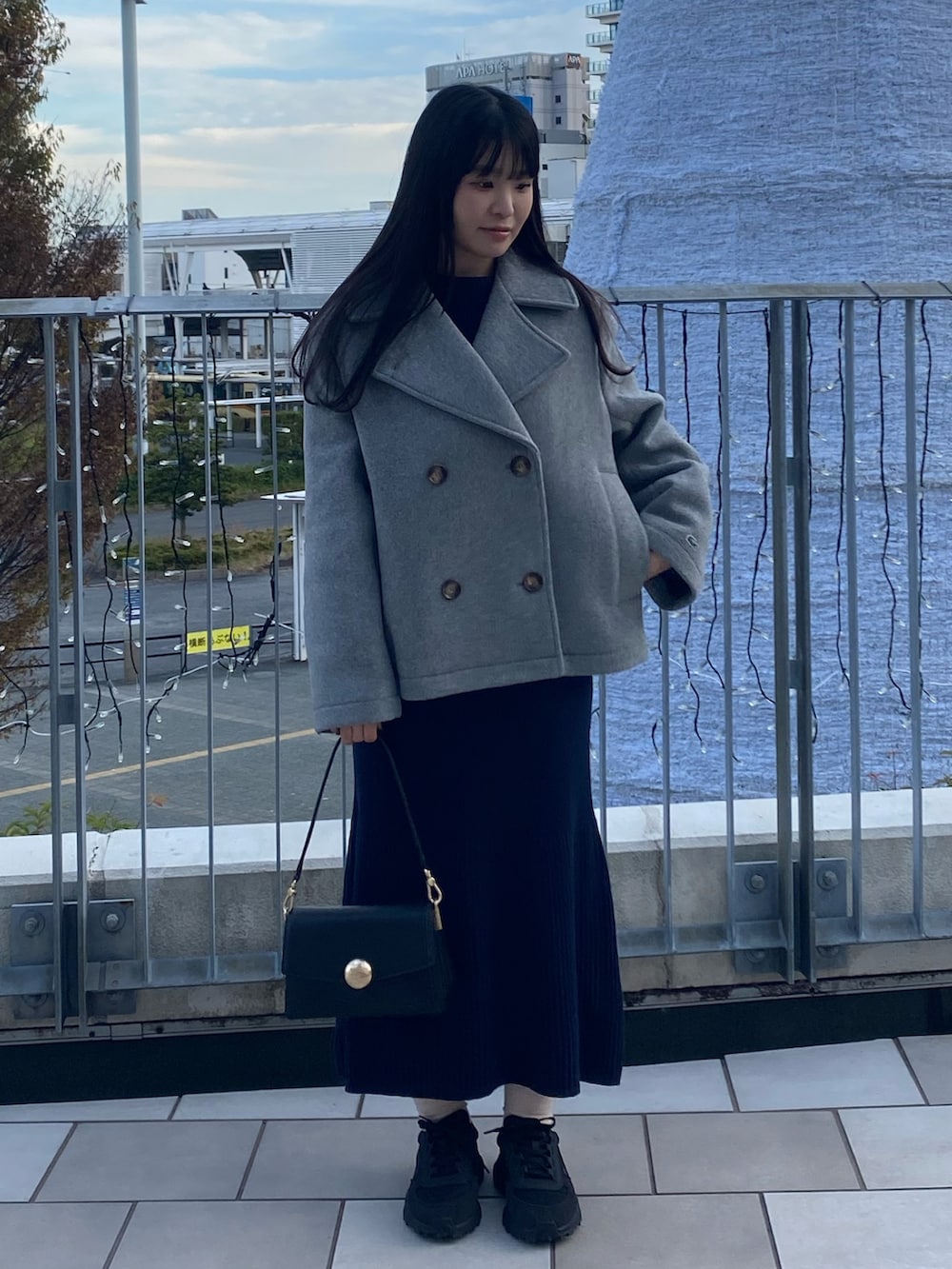 グレー系のピーコート、ブルー系のワンピース、ブラック系のバッグを着用したレディースの冬コーディネートの2枚目の写真