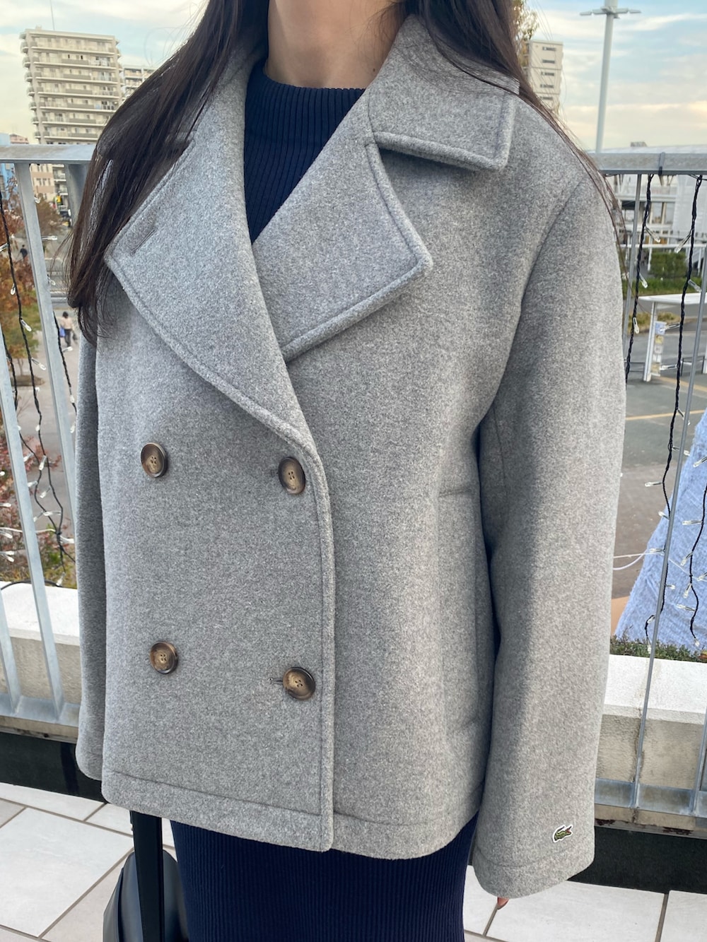 グレー系のピーコート、ブルー系のワンピース、ブラック系のバッグを着用したレディースの冬コーディネートの4枚目の写真