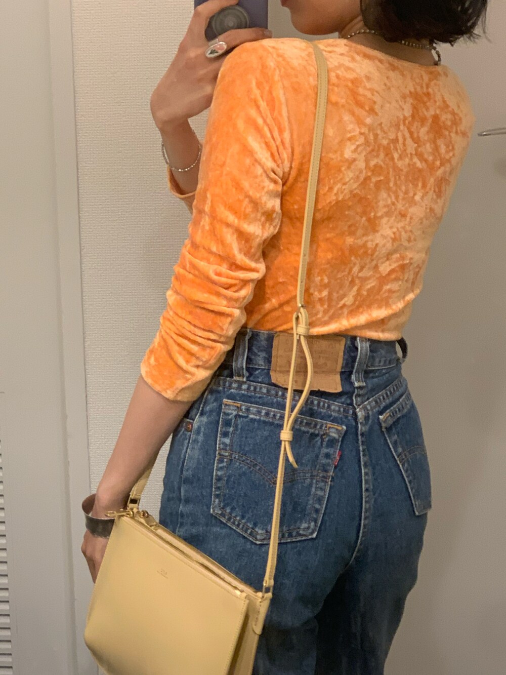 オレンジ系のTシャツ/カットソー、ベージュ系のショルダーバッグ、ブルー系のデニムパンツを着用したレディースの春コーディネートの2枚目の写真