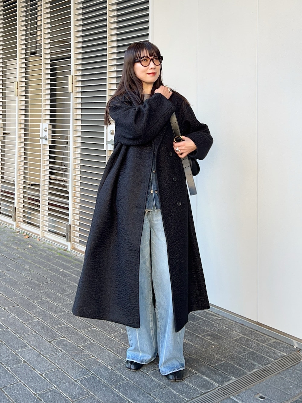 ブラック系のステンカラーコート、その他のベスト、ブルー系のデニムパンツを着用したレディースの冬コーディネートの2枚目の写真