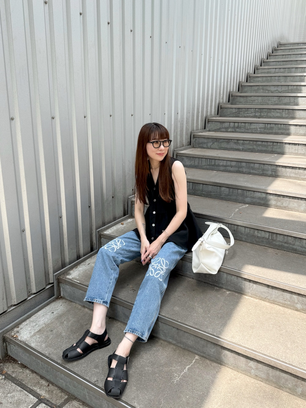 ブラック系のニット/セーター、ブラック系のサンダル、ブルー系のデニムパンツを着用したレディースの夏コーディネートの5枚目の写真