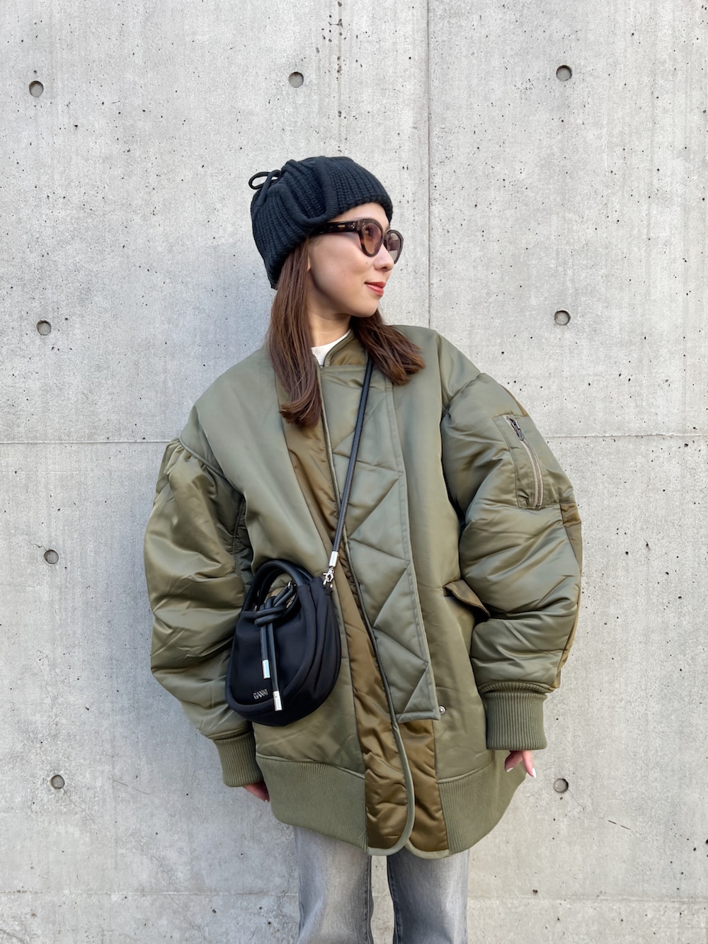 グリーン系のブルゾン、ブラック系のハンドバッグ、グレー系のデニムパンツを着用したレディースの冬コーディネートの5枚目の写真