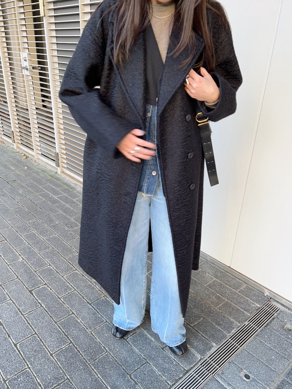 ブラック系のステンカラーコート、その他のベスト、ブルー系のデニムパンツを着用したレディースの冬コーディネートの5枚目の写真