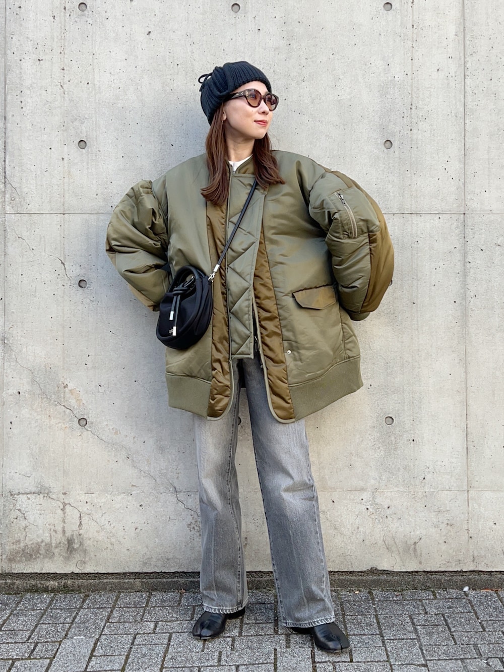 グリーン系のブルゾン、ブラック系のハンドバッグ、グレー系のデニムパンツを着用したレディースの冬コーディネートの2枚目の写真