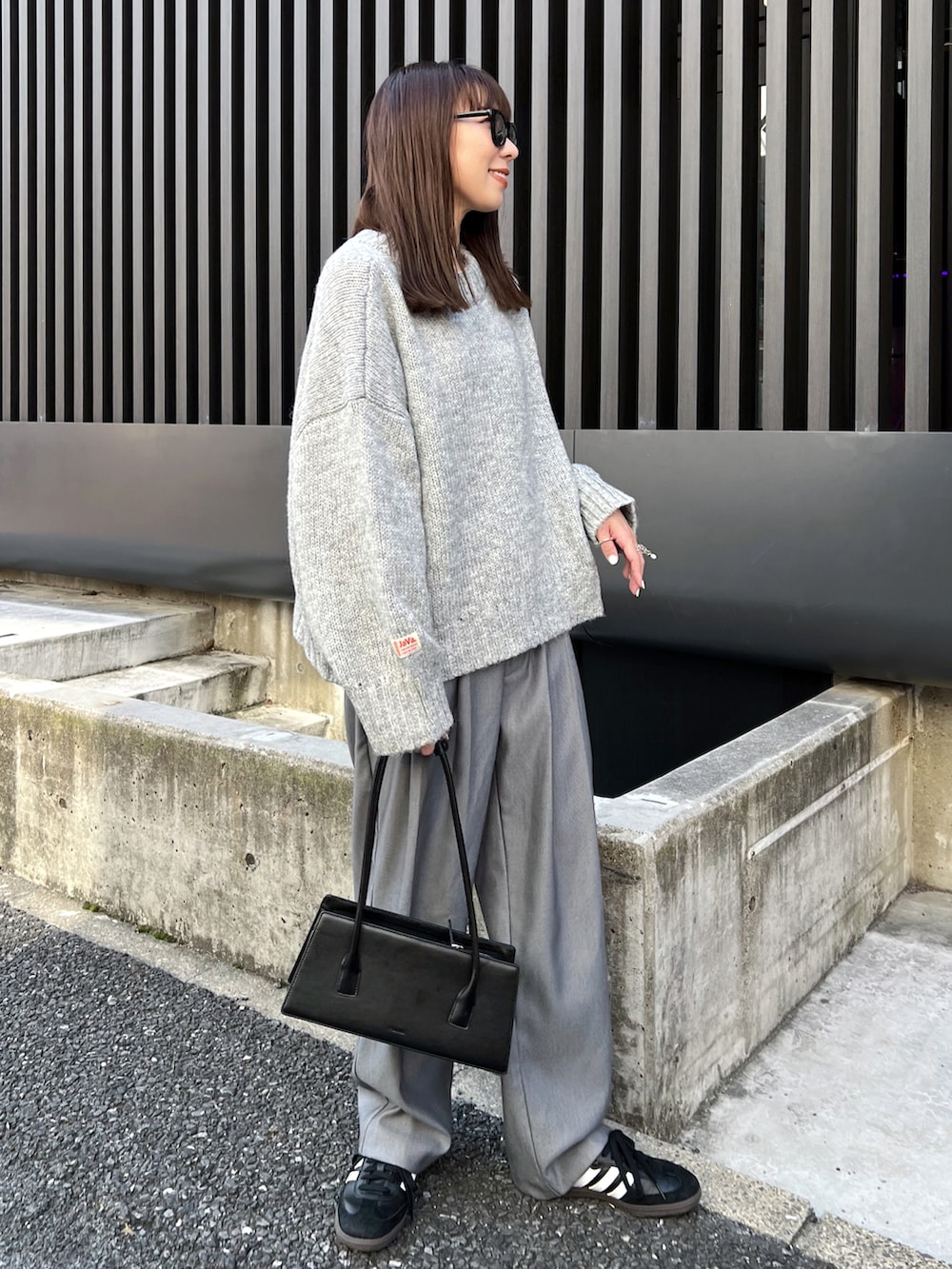 グレー系のニット/セーター、グレー系のスラックス、ブラック系のスニーカーを着用したレディースの秋コーディネートの2枚目の写真