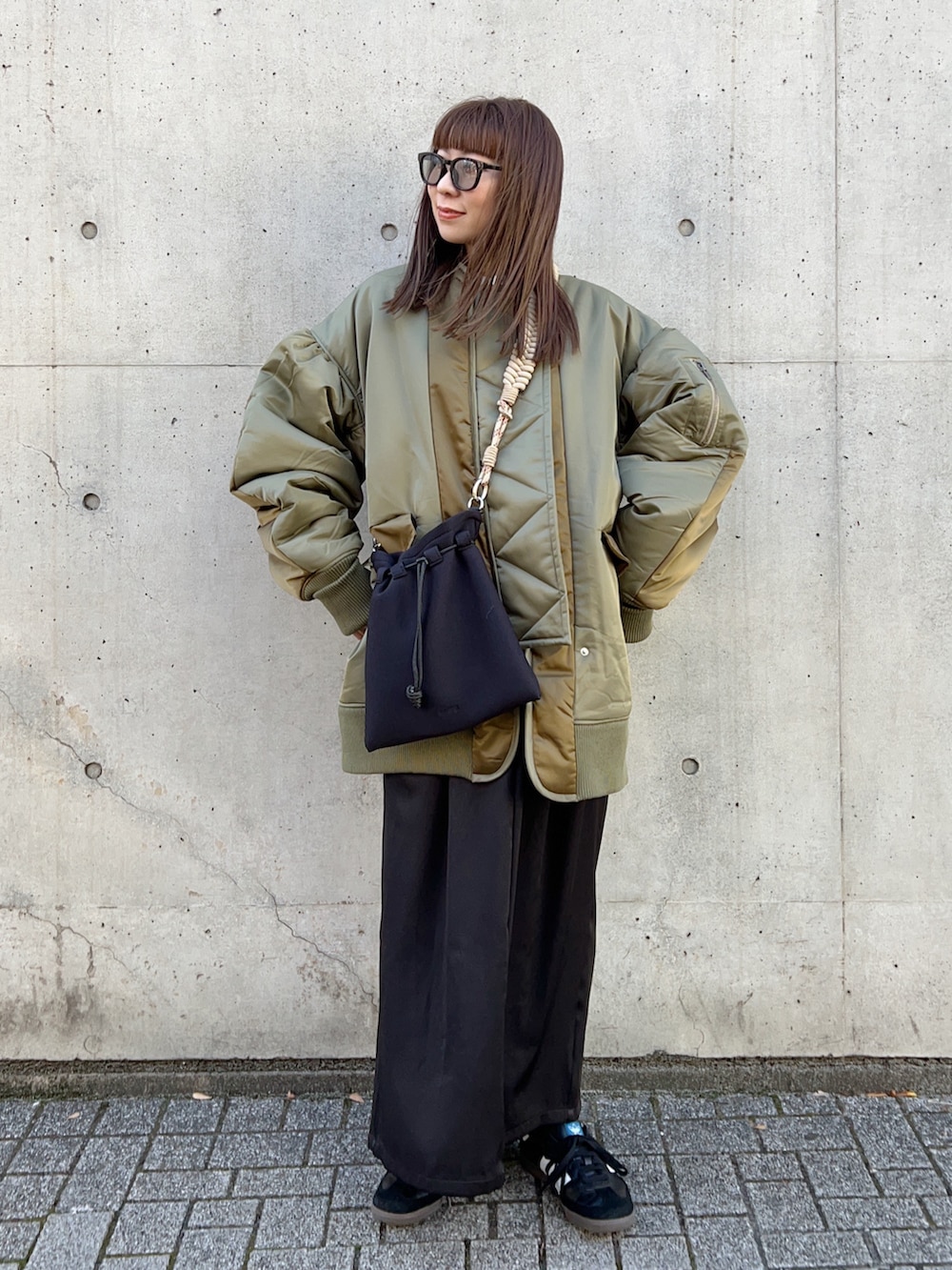 グリーン系のブルゾン、ベージュ系のショルダーバッグ、ブラック系のワンピースを着用したレディースの冬コーディネートの2枚目の写真