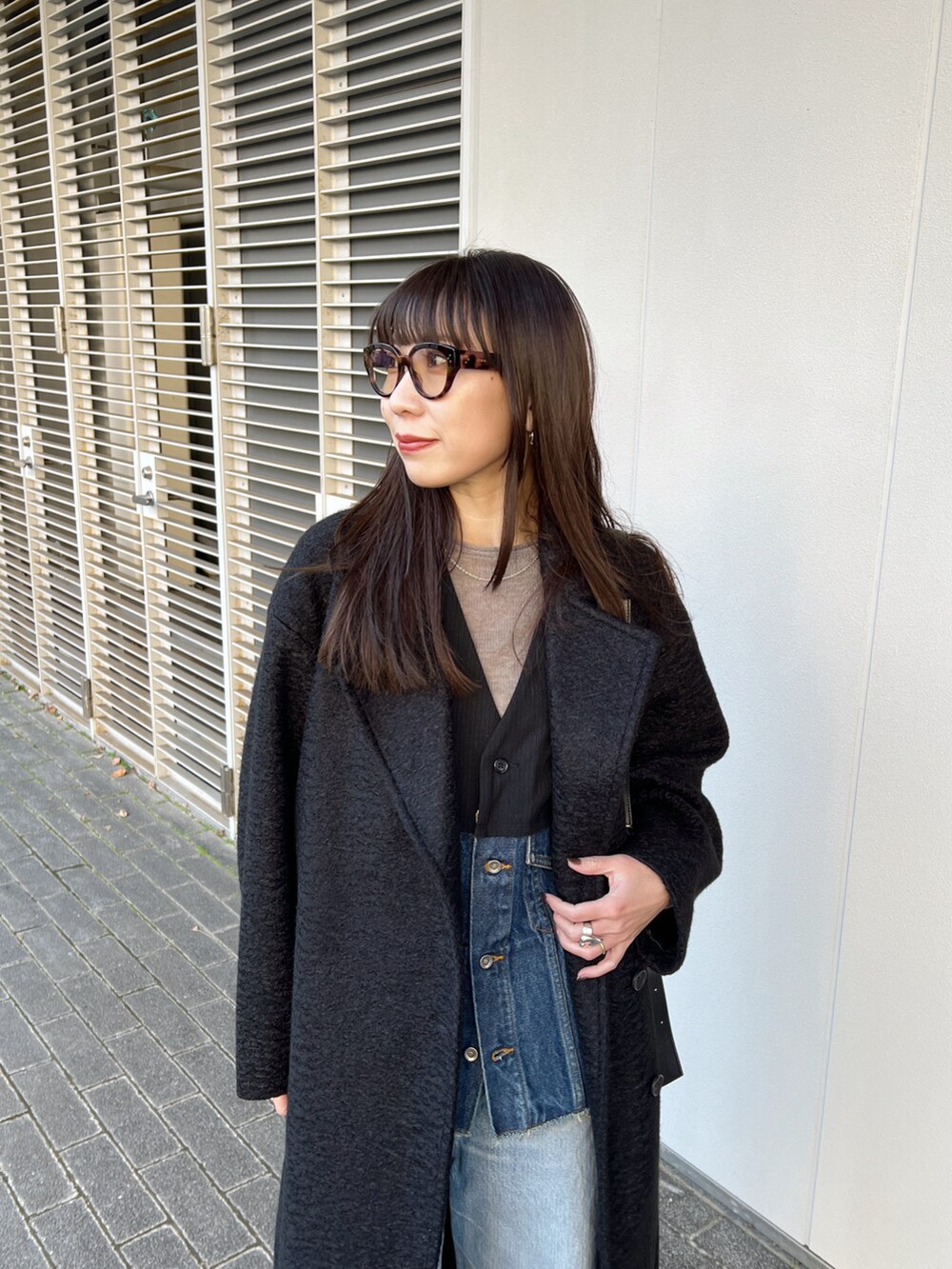 ブラック系のステンカラーコート、その他のベスト、ブルー系のデニムパンツを着用したレディースの冬コーディネートの4枚目の写真