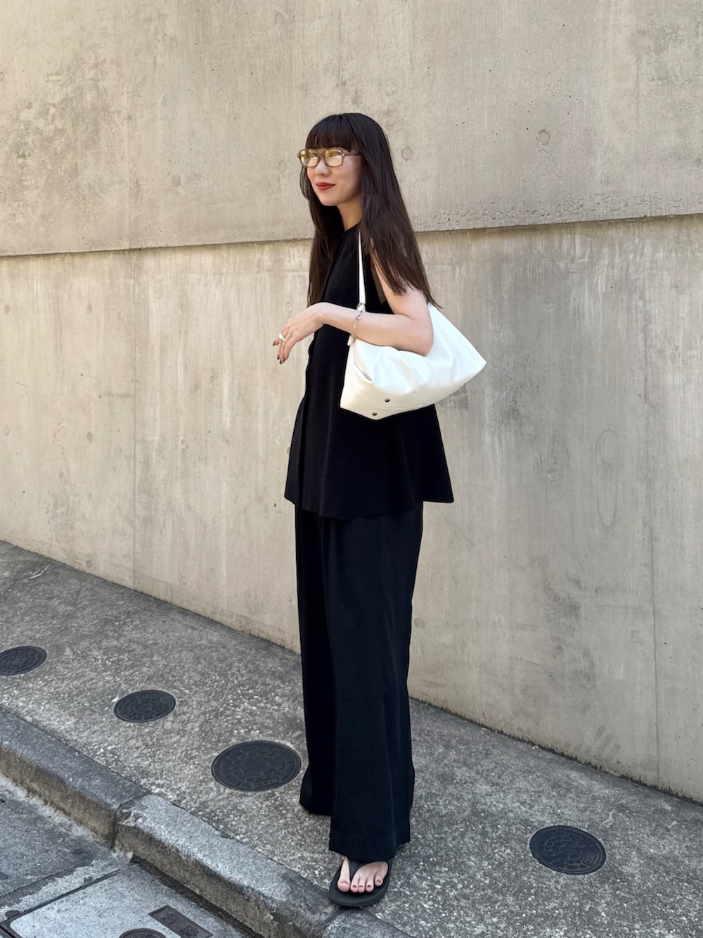 ブラック系のベスト、ブラック系のスラックス、ホワイト系のバッグを着用したレディースの夏コーディネートの3枚目の写真