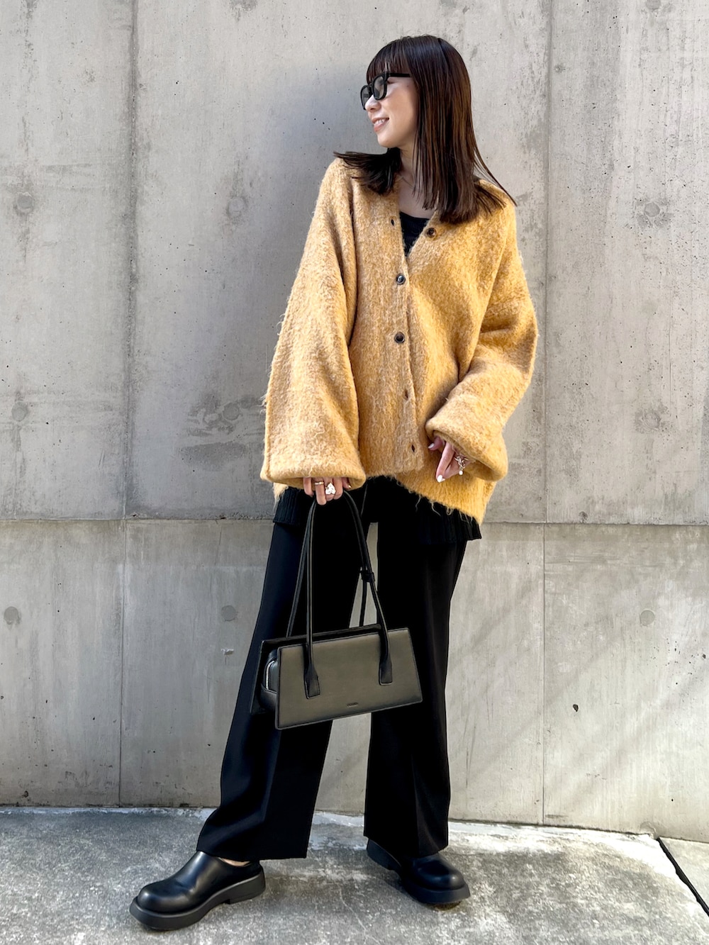 イエロー系のカーディガン/ボレロ、ブラック系のスラックス、ブラック系のハンドバッグを着用したレディースの秋コーディネートの2枚目の写真