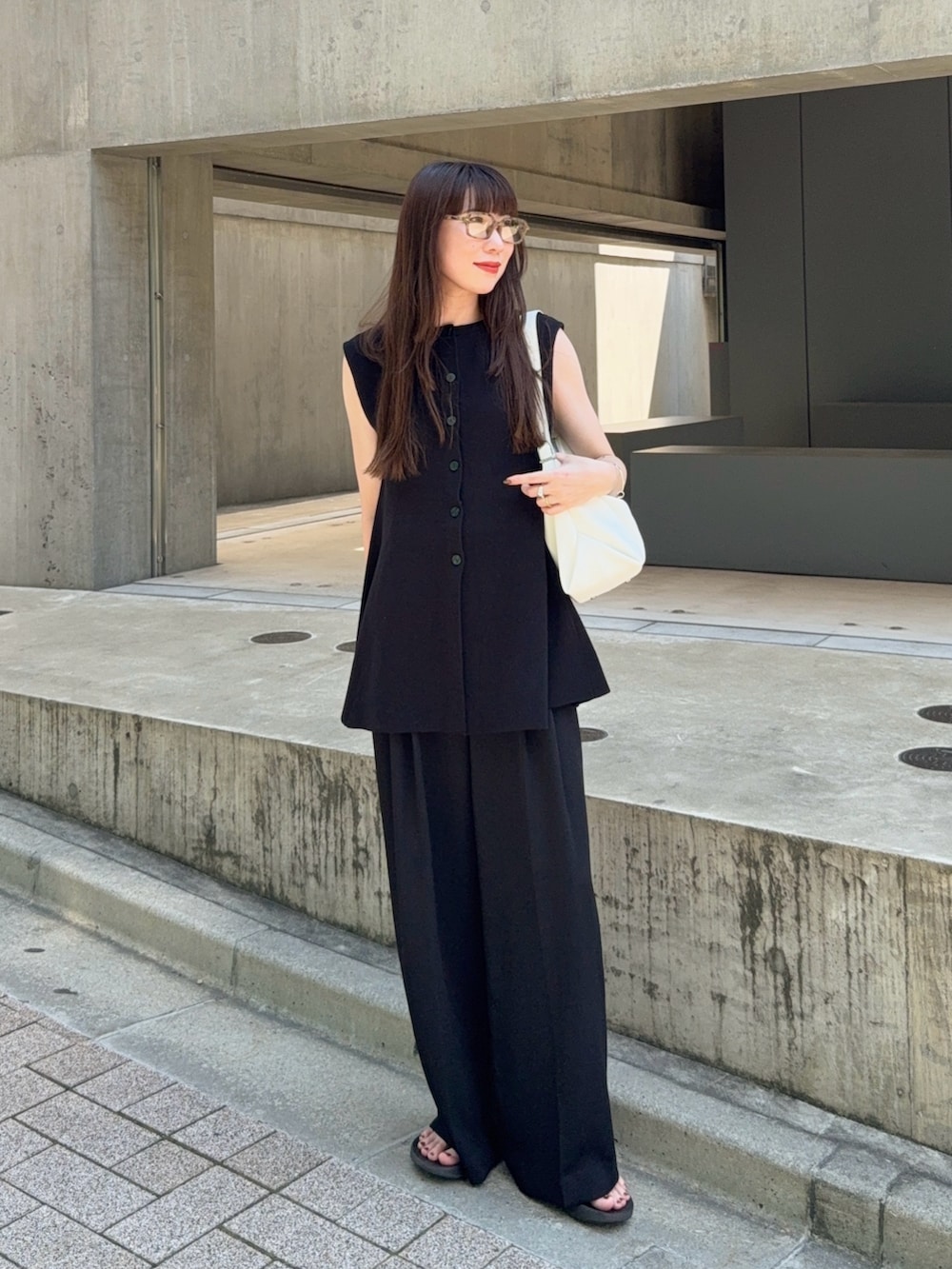 ブラック系のベスト、ブラック系のスラックス、ホワイト系のバッグを着用したレディースの夏コーディネートの2枚目の写真