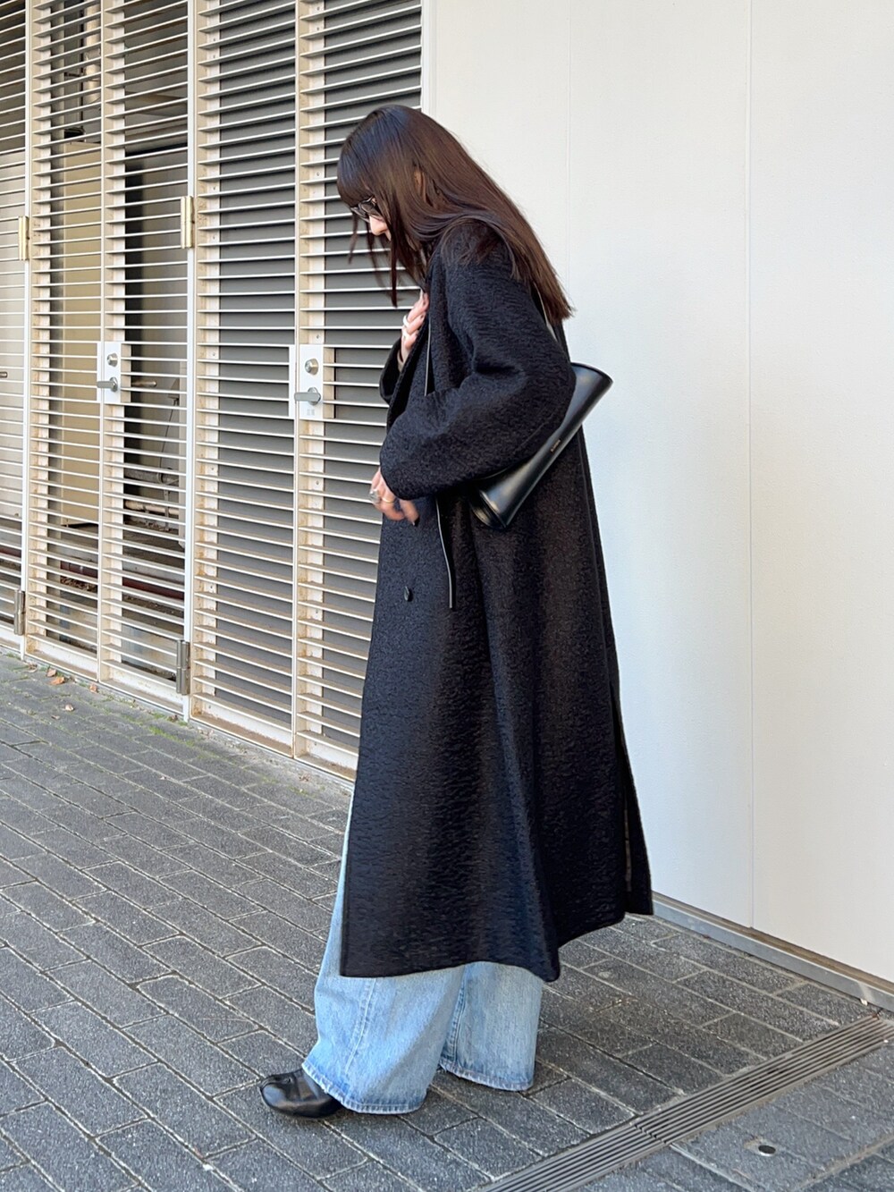 ブラック系のステンカラーコート、その他のベスト、ブルー系のデニムパンツを着用したレディースの冬コーディネートの3枚目の写真
