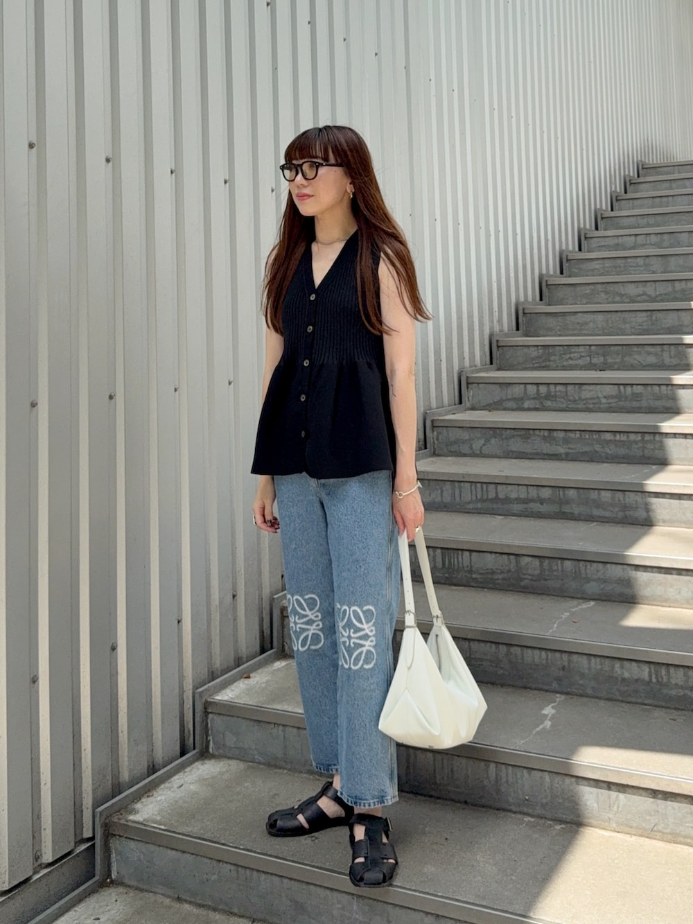 ブラック系のニット/セーター、ブラック系のサンダル、ブルー系のデニムパンツを着用したレディースの夏コーディネートの4枚目の写真