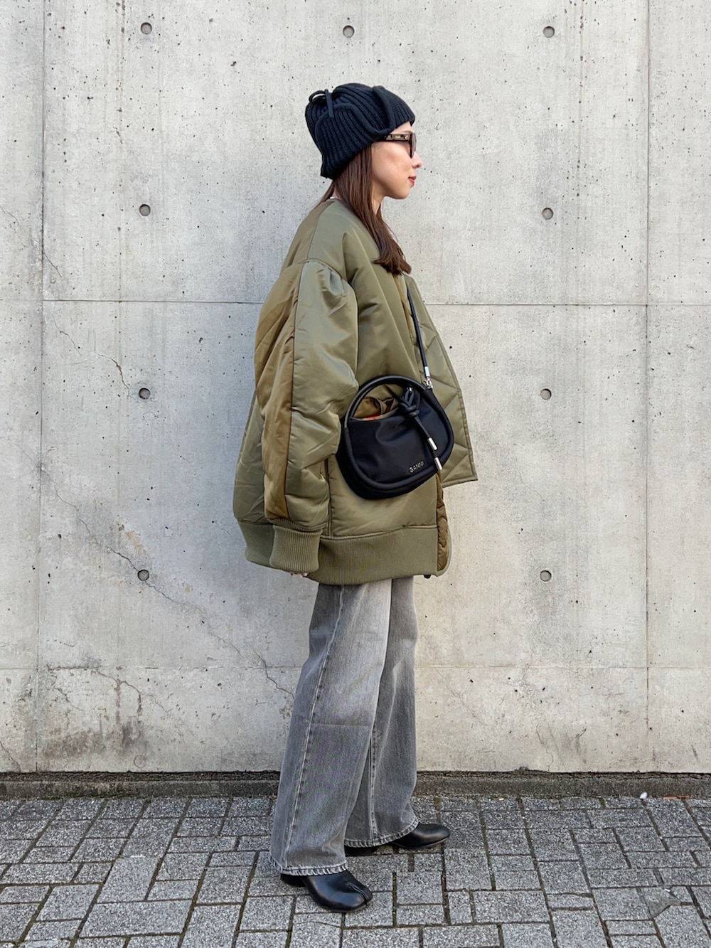 グリーン系のブルゾン、ブラック系のハンドバッグ、グレー系のデニムパンツを着用したレディースの冬コーディネートの4枚目の写真