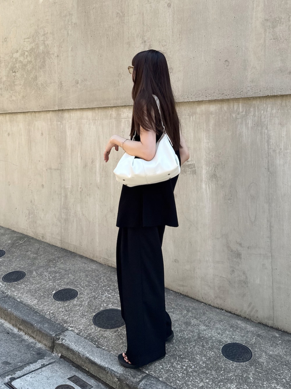 ブラック系のベスト、ブラック系のスラックス、ホワイト系のバッグを着用したレディースの夏コーディネートの5枚目の写真